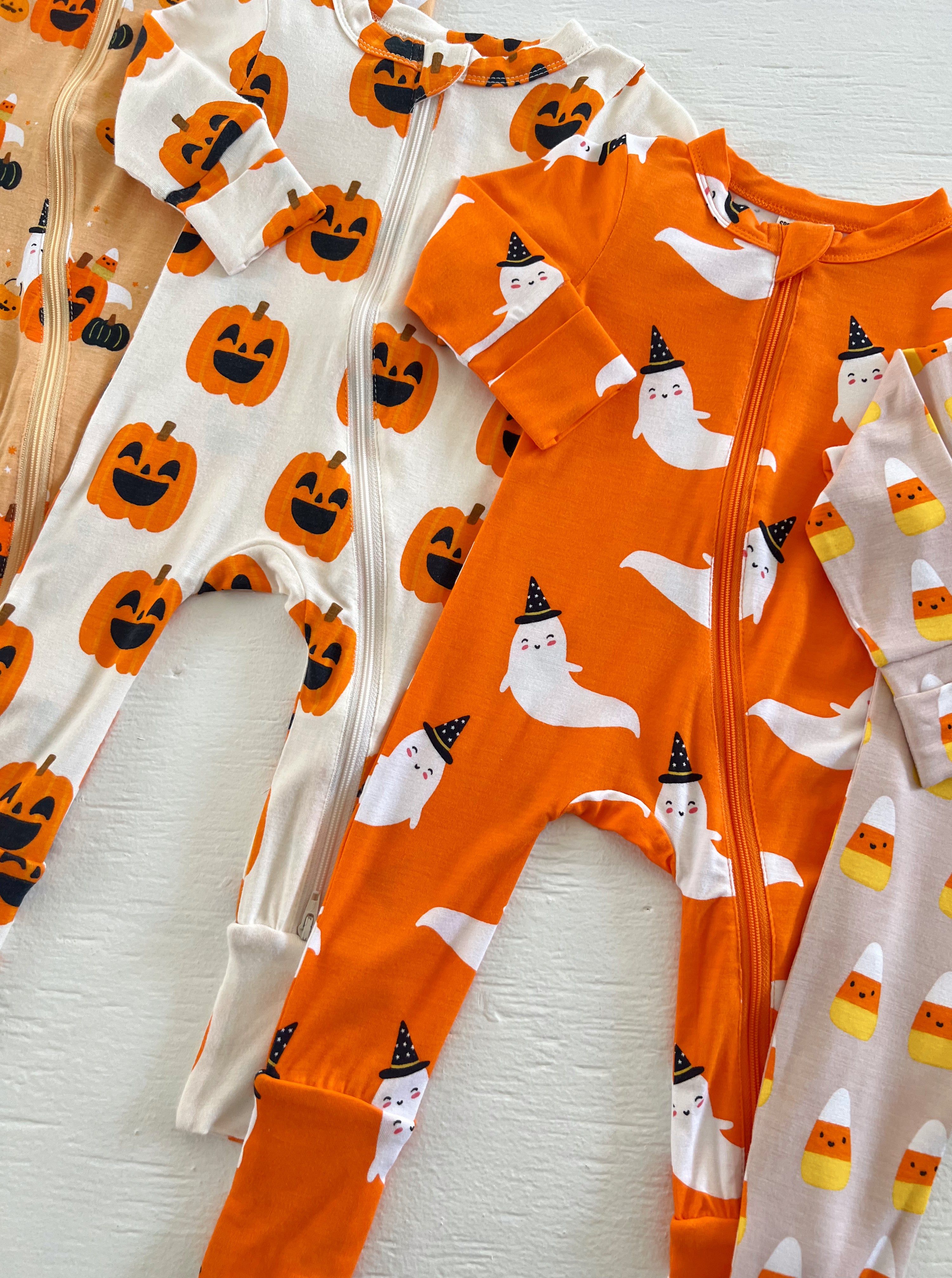 Colorful Halloween-themed baby onesies featuring pumpkins, ghosts, and candy corn patterns.
