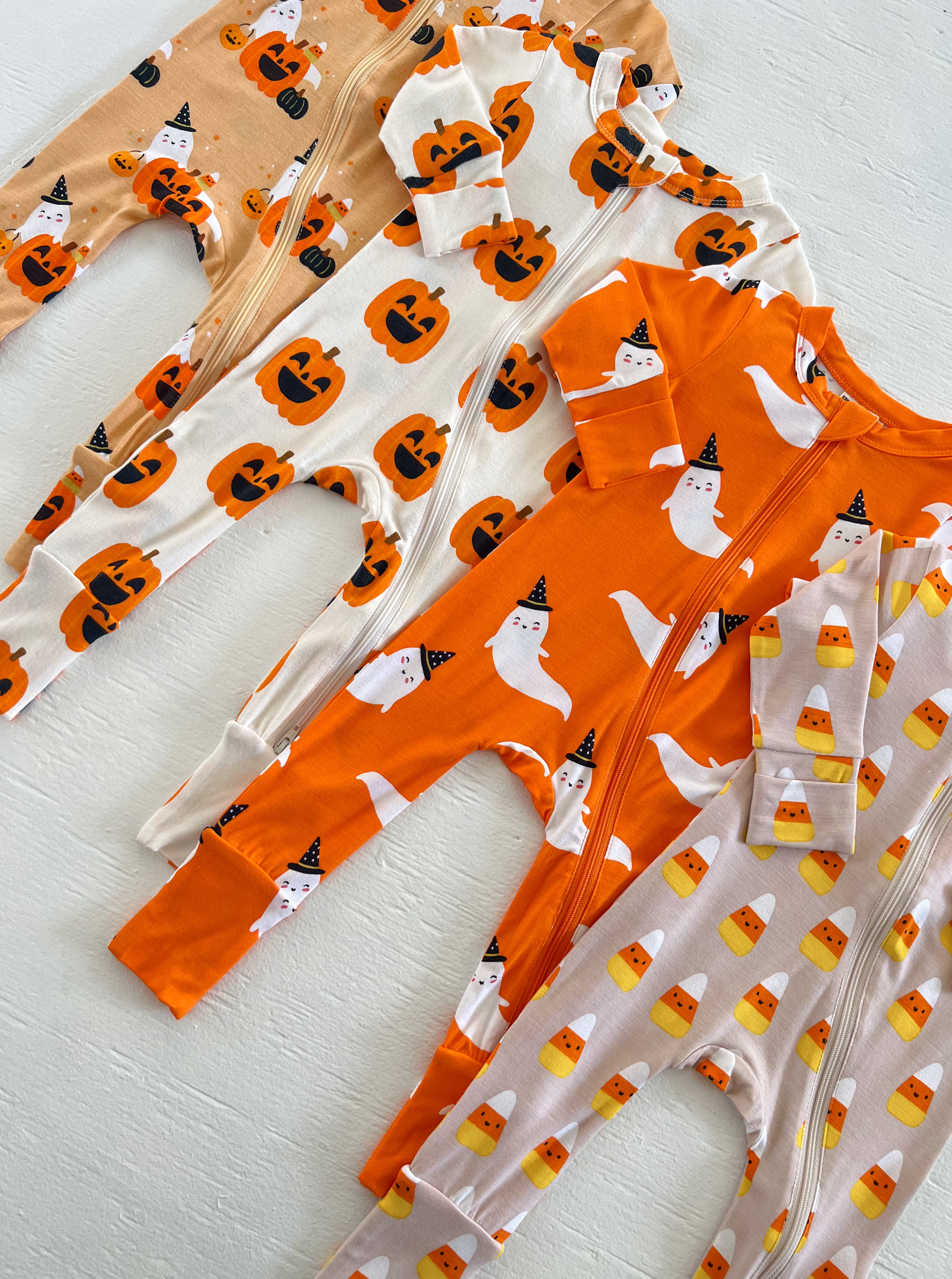 Four Halloween-themed onesies featuring pumpkins, ghosts, and candy corn on a light background.