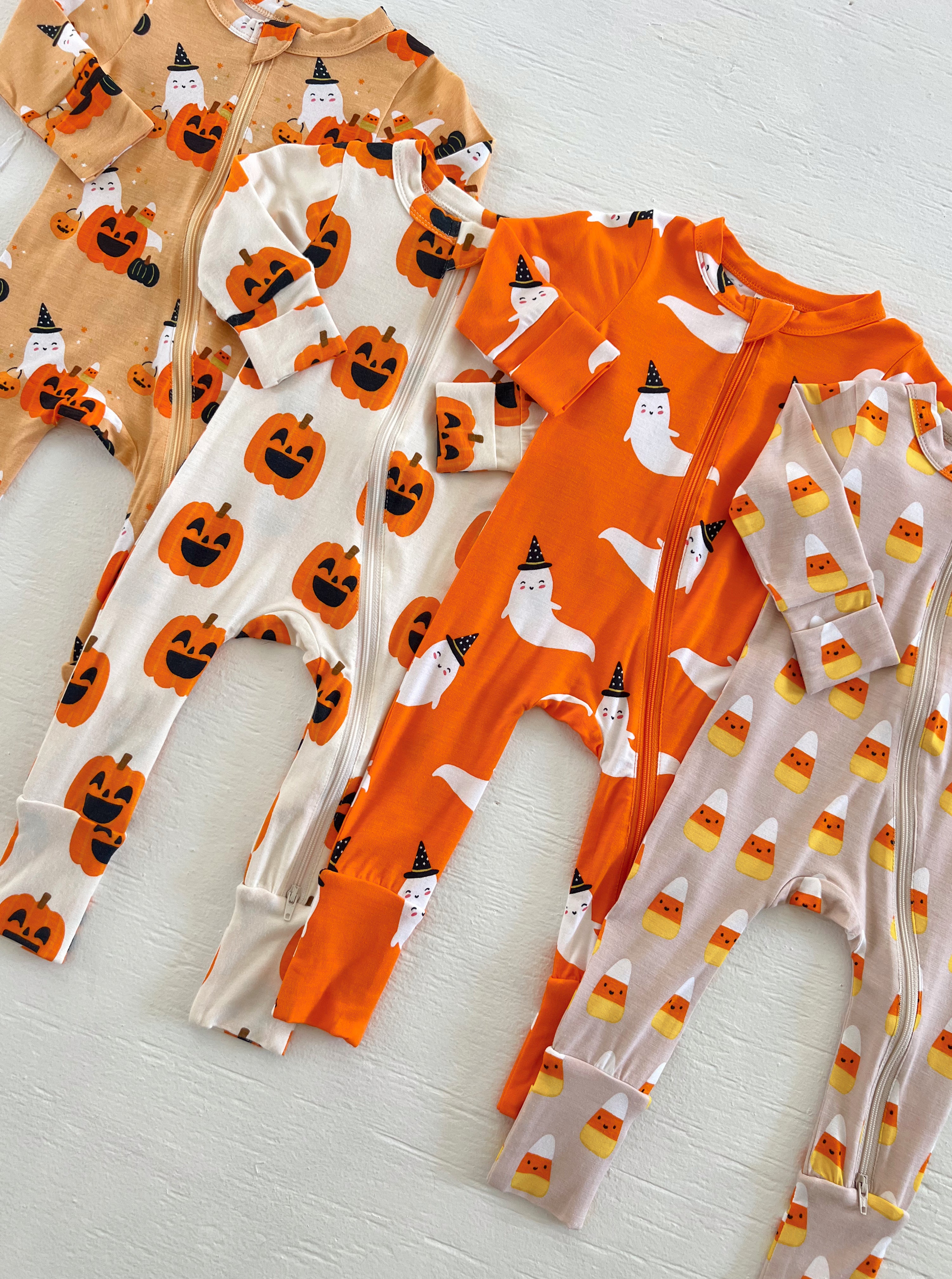 Colorful Halloween-themed pajamas featuring pumpkins, ghosts, and candy corn patterns on a light background.