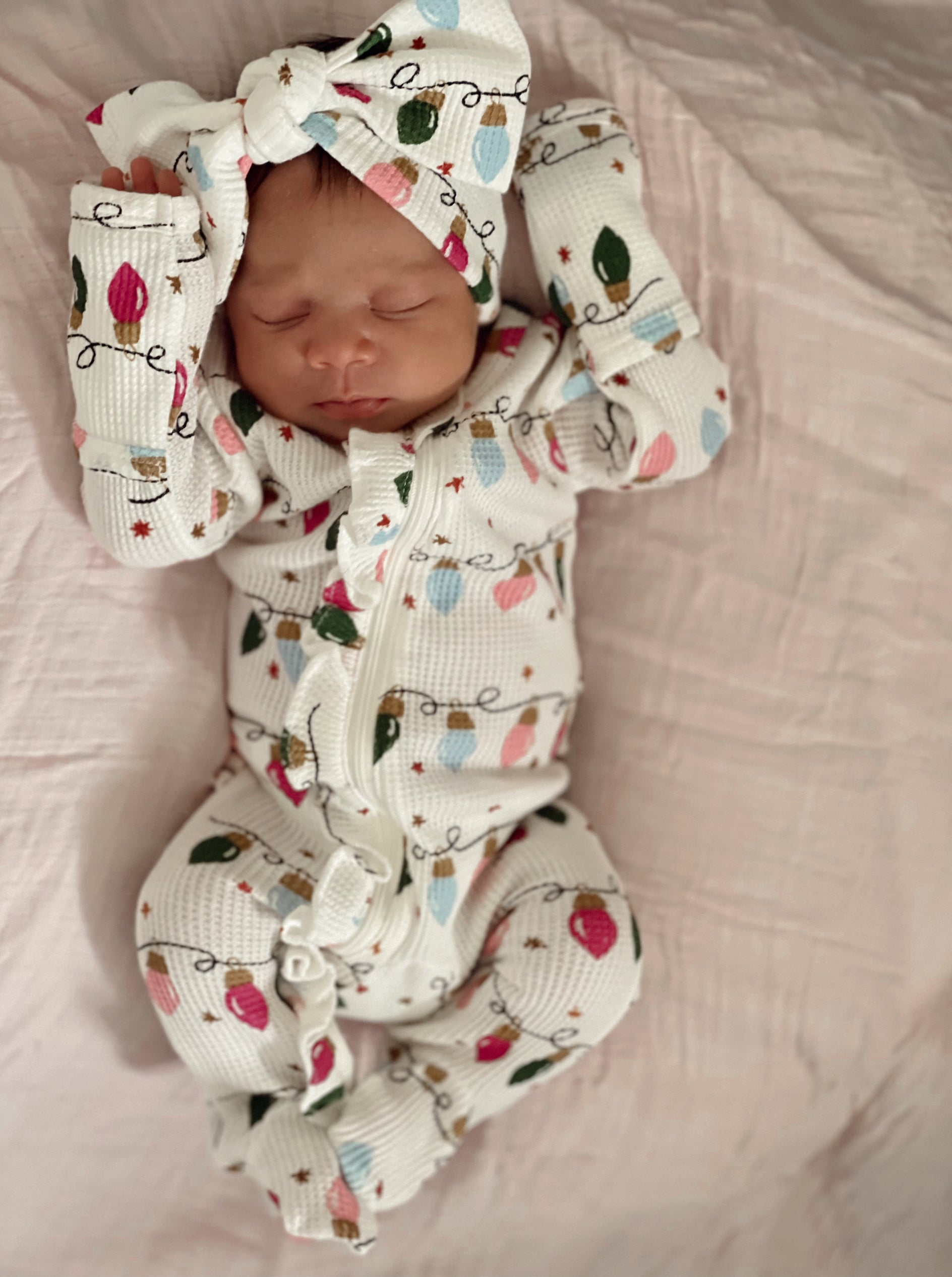Baby sleeping on a soft blanket, wearing a festive outfit with colorful lights and a matching headband.