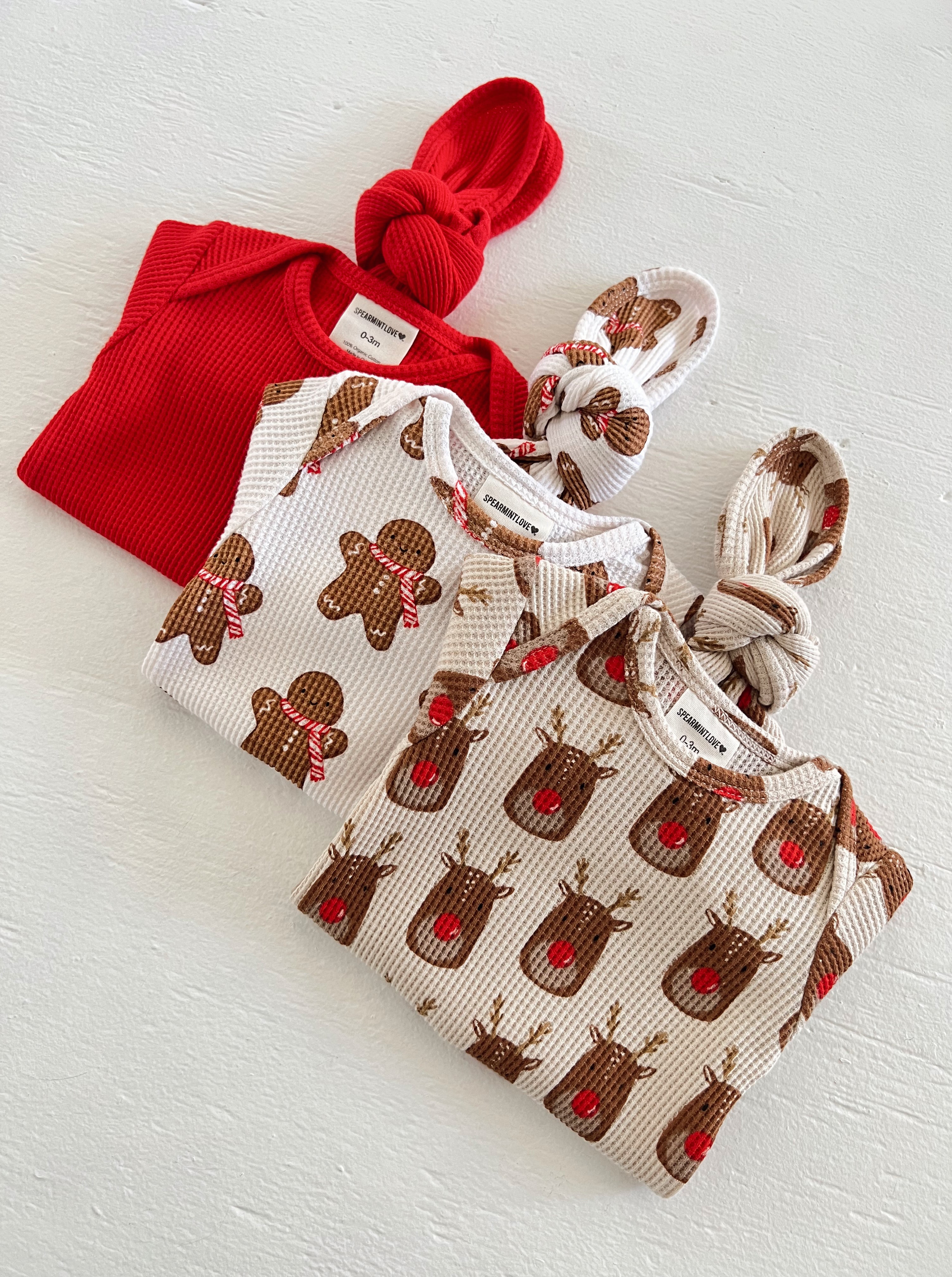 Three holiday-themed infant outfits: red top, and patterned tops featuring gingerbread and reindeer designs.