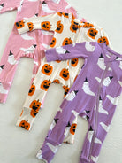 Three colorful children's onesies with ghost and pumpkin patterns on a textured white background.