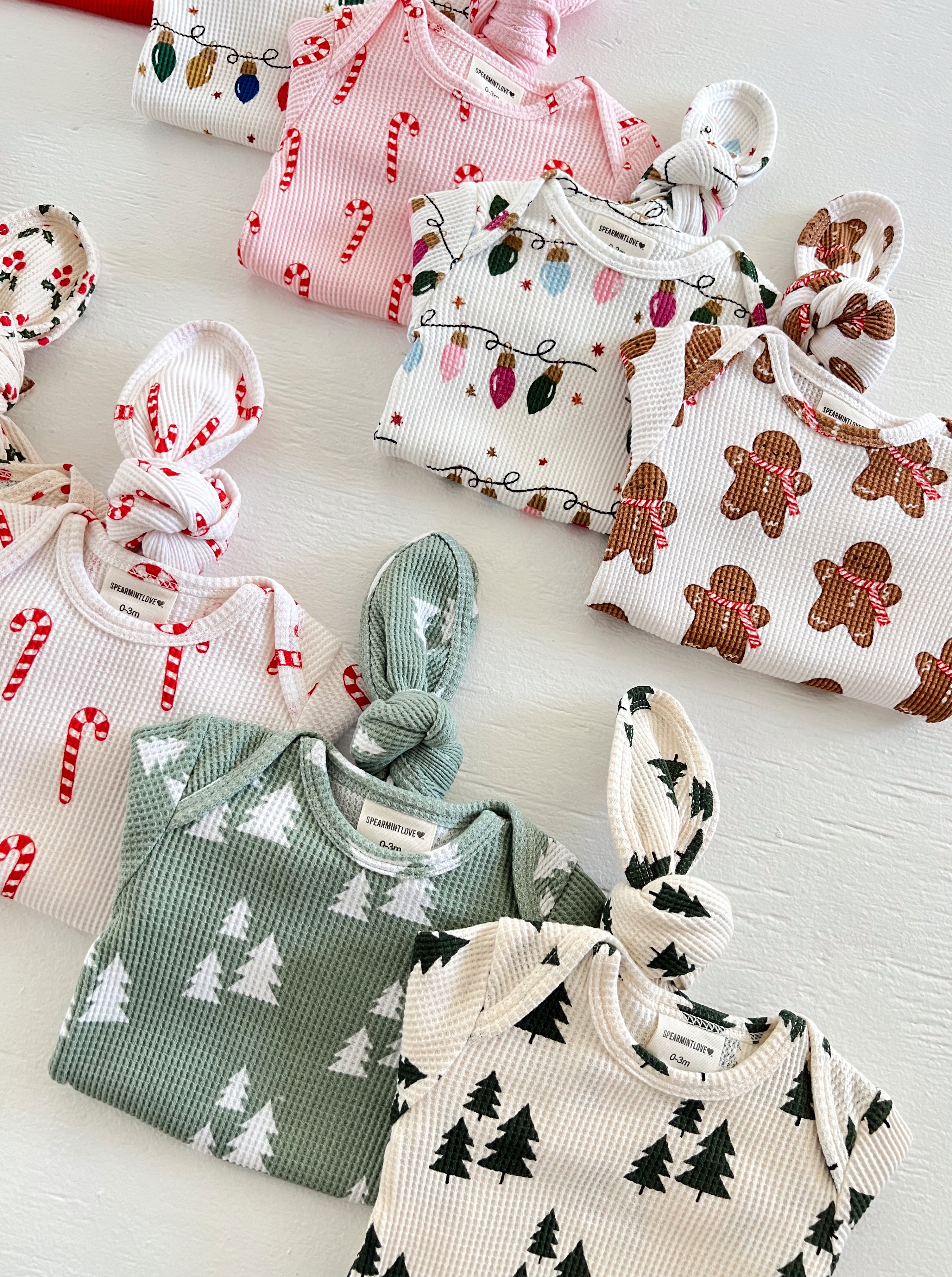 Colorful baby outfits with festive patterns including candy canes, Christmas lights, gingerbread, and trees.