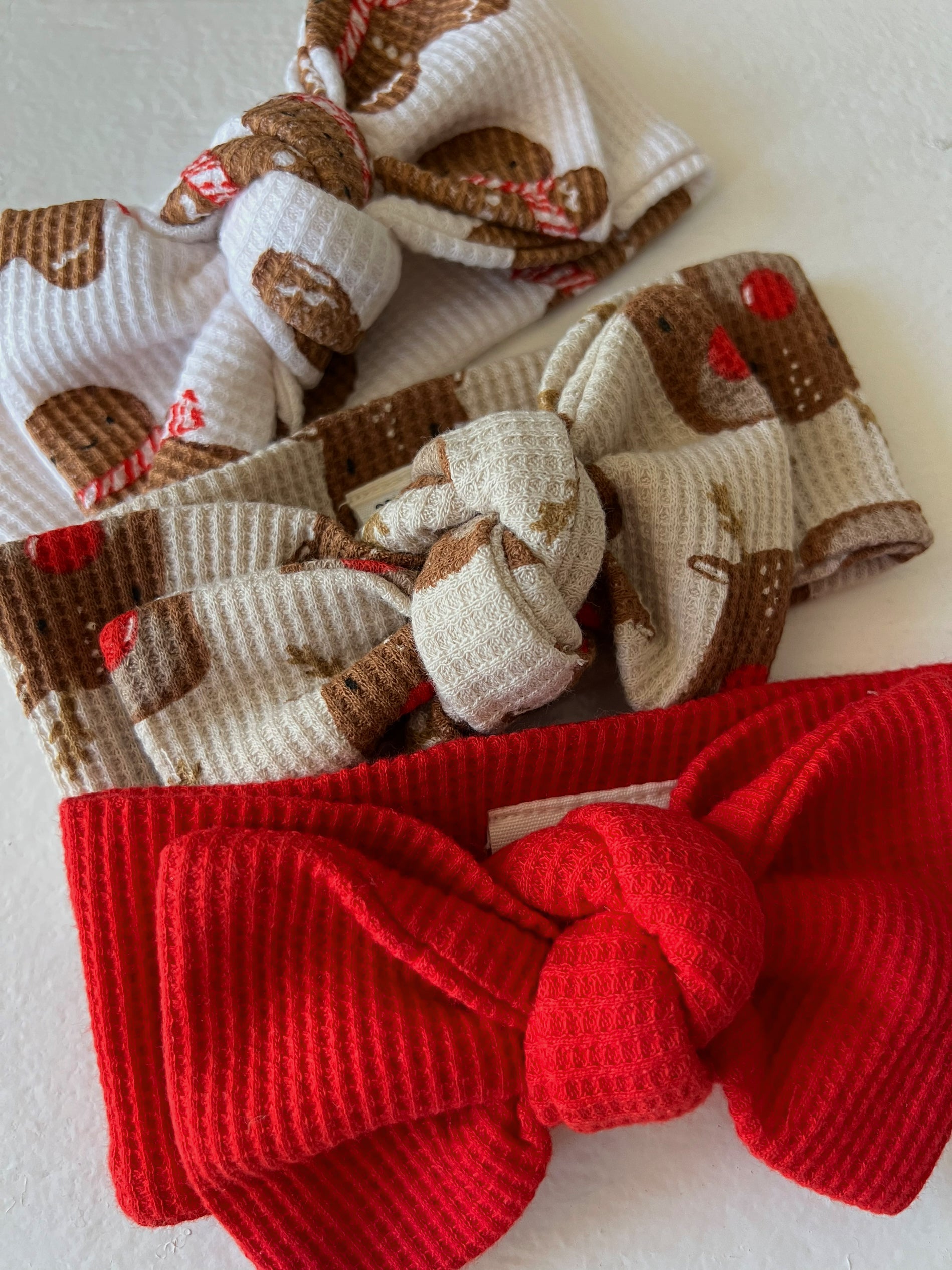 Three fabric headbands: one with gingerbread pattern, one cream, and a bold red one with a large bow.