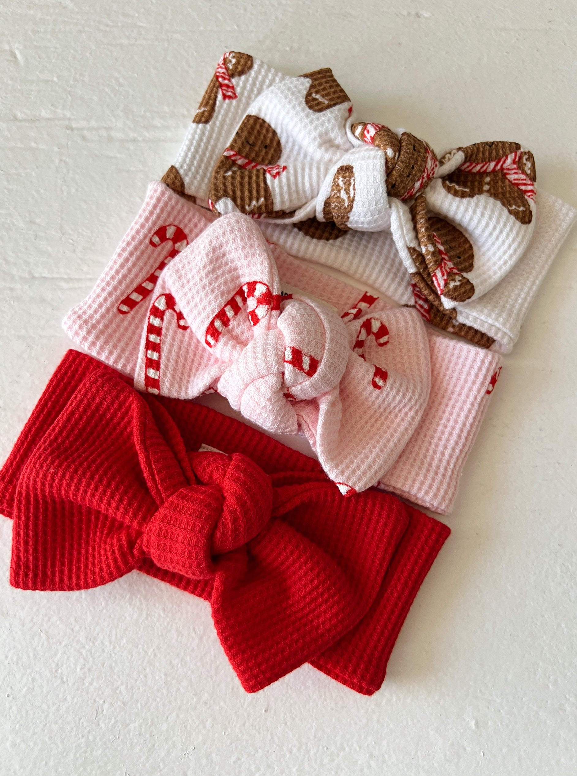 Three festive headbands: red, pink with candy canes, and white with gingerbread cookies. Perfect for holiday styling.