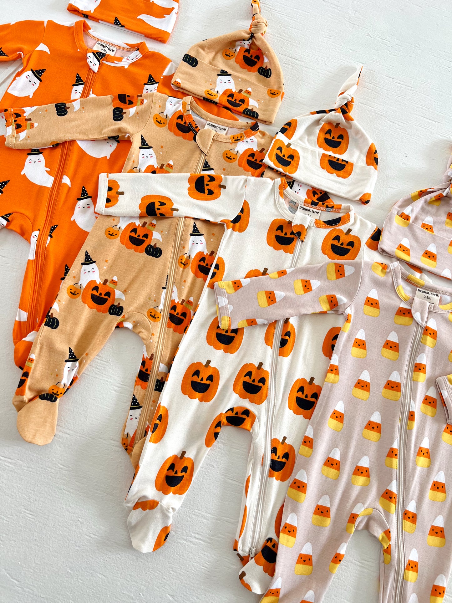 Colorful Halloween baby outfits with pumpkin and ghost designs, including hats in a playful arrangement.