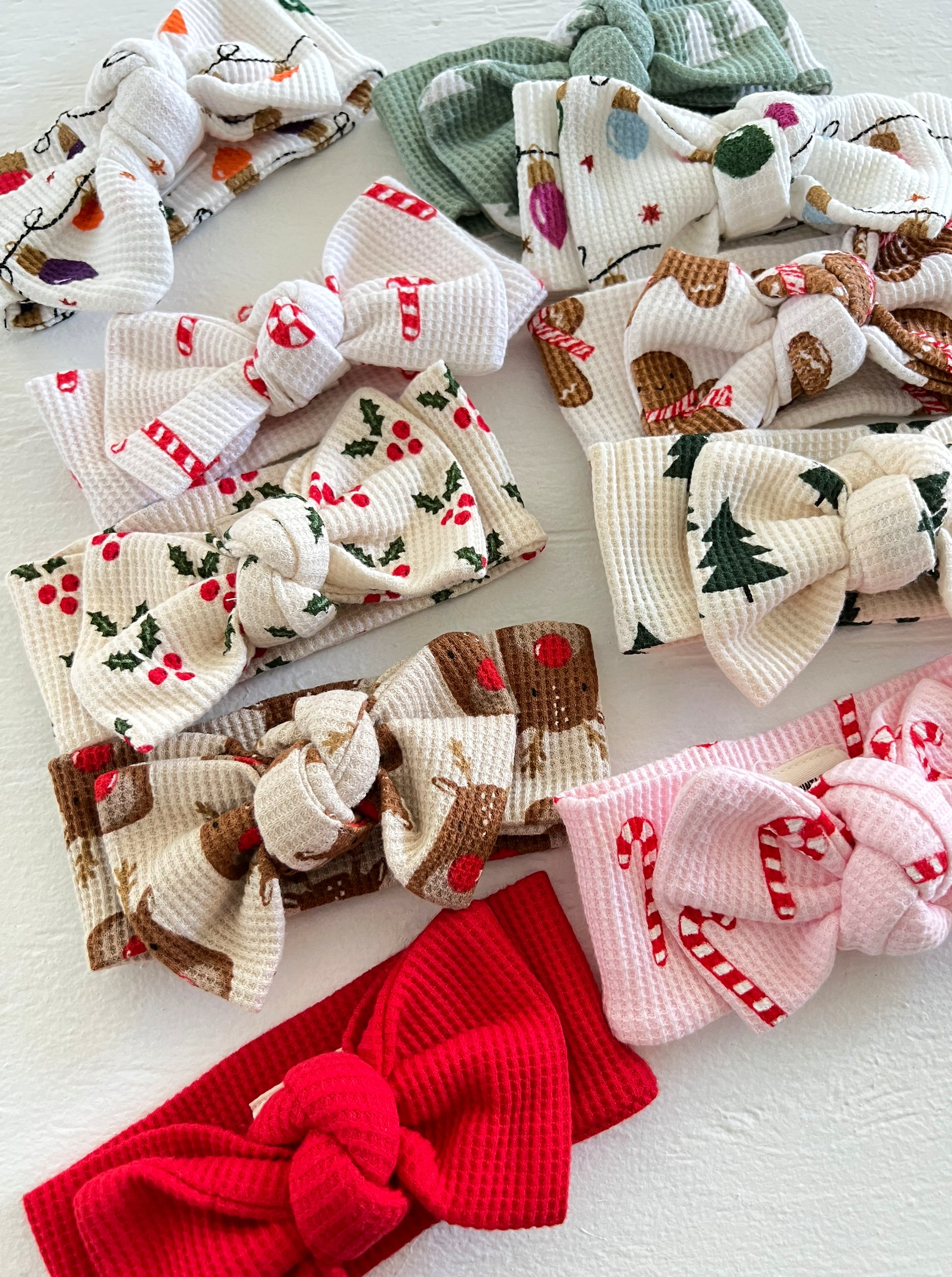 A collection of colorful fabric headbands with festive holiday patterns and bows arranged on a light background.