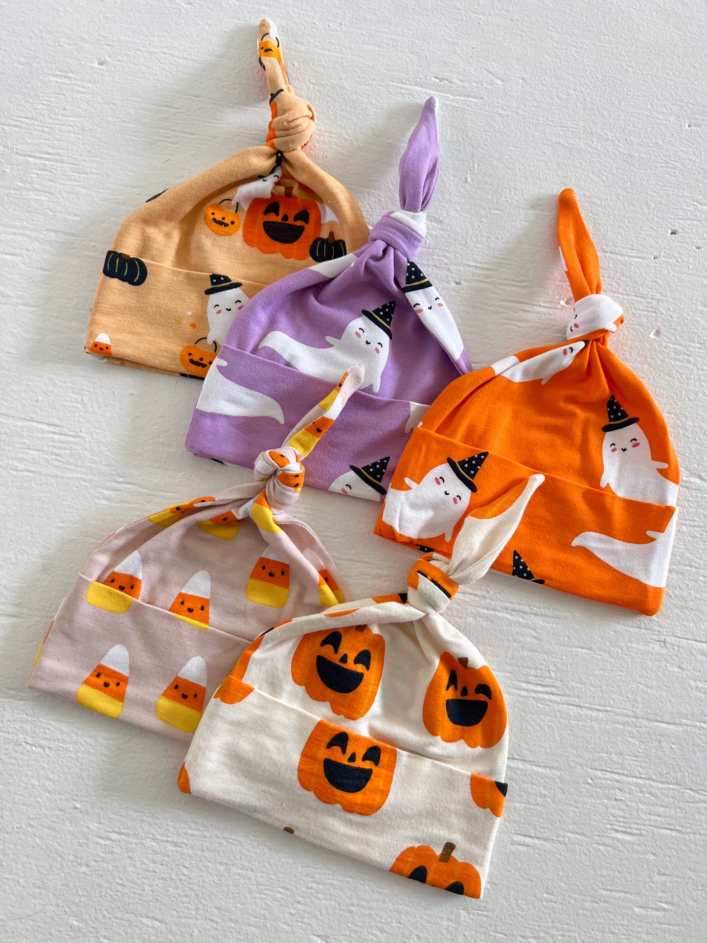 Five colorful Halloween-themed baby hats with various designs, including pumpkins and ghosts, arranged on a white surface.