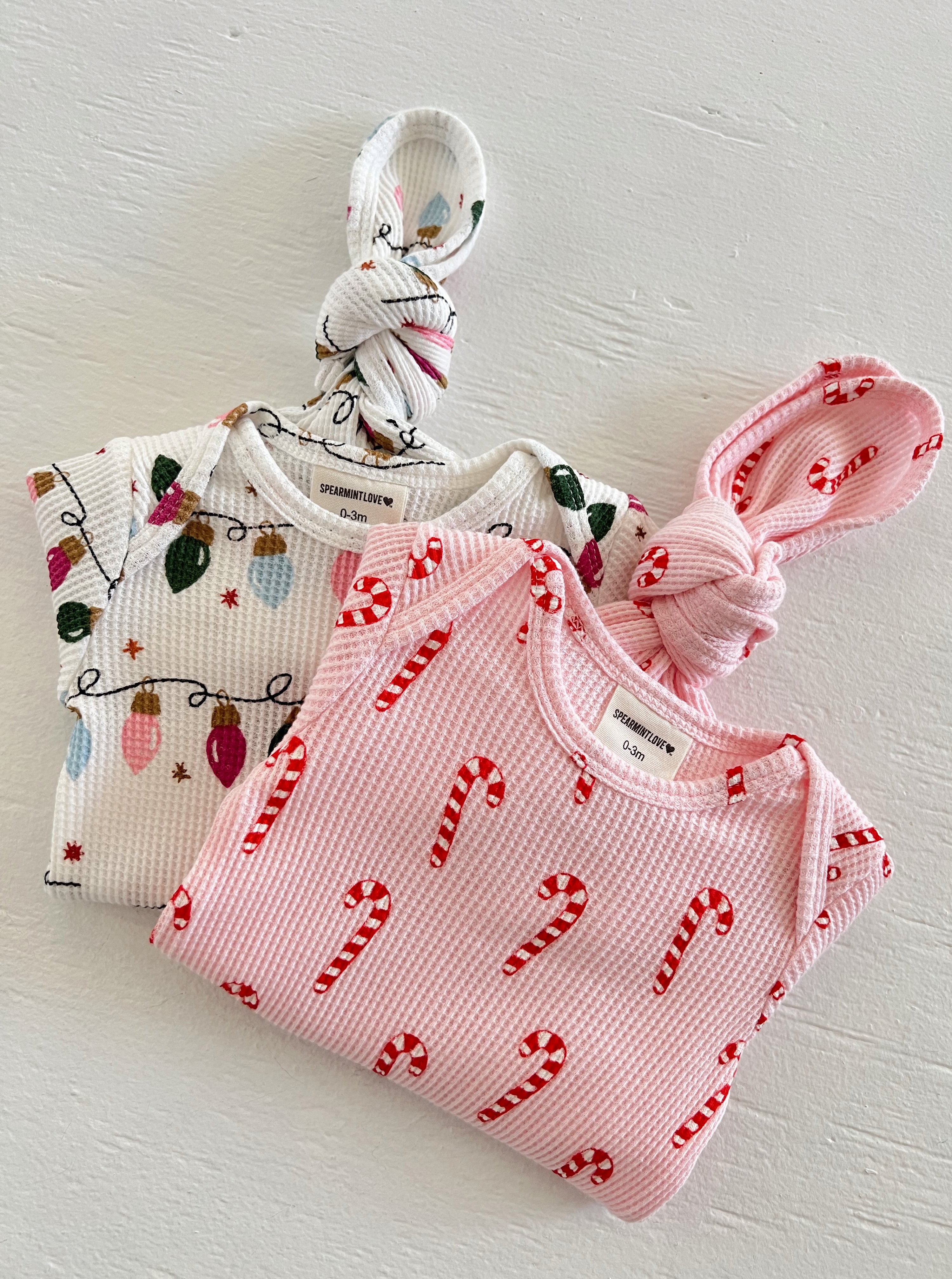 Two baby knotted gowns: one with holiday lights, the other with candy canes, on a light background.