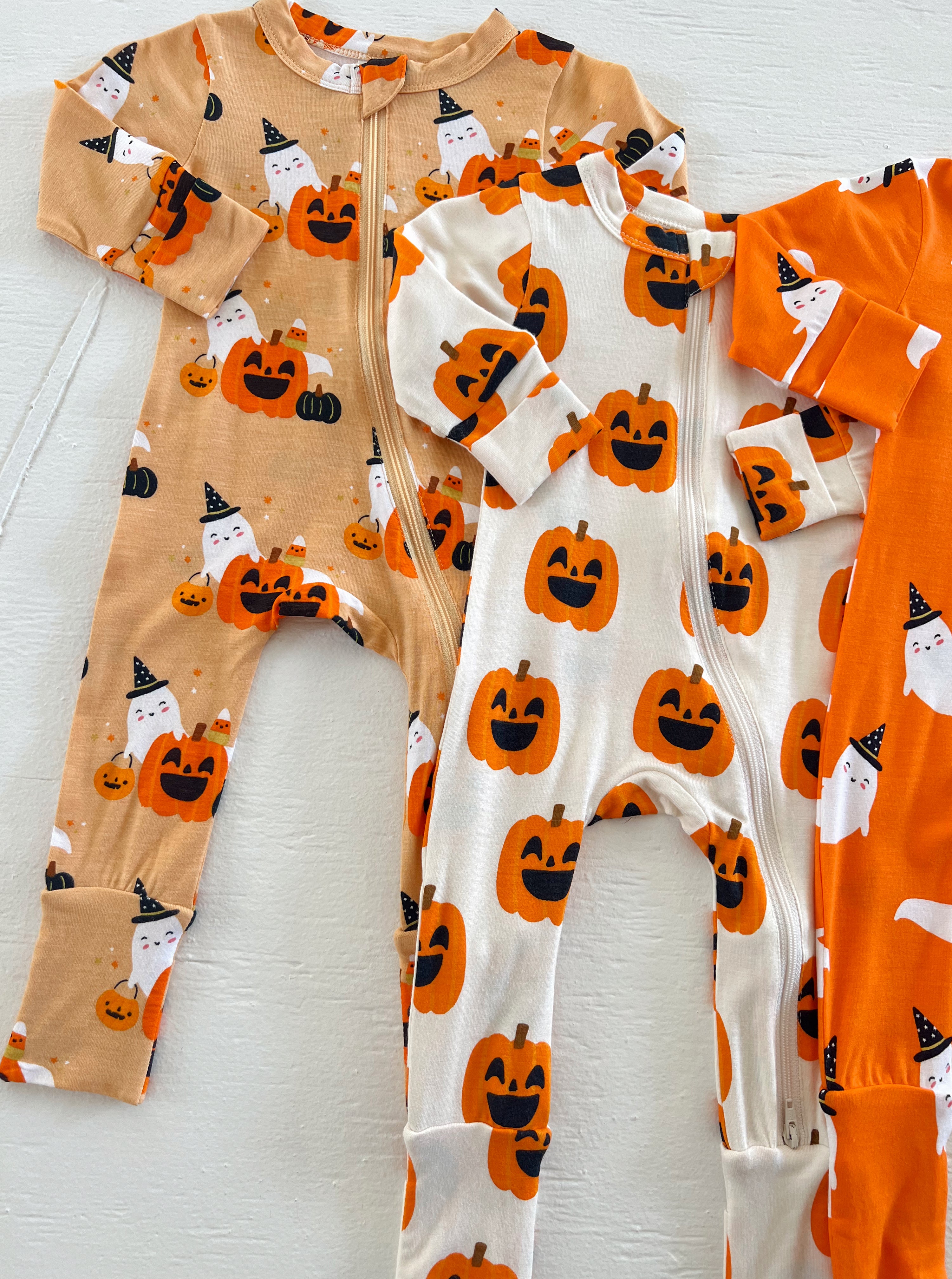 Assorted Halloween-themed baby onesies with pumpkins and ghosts in orange and beige colors.