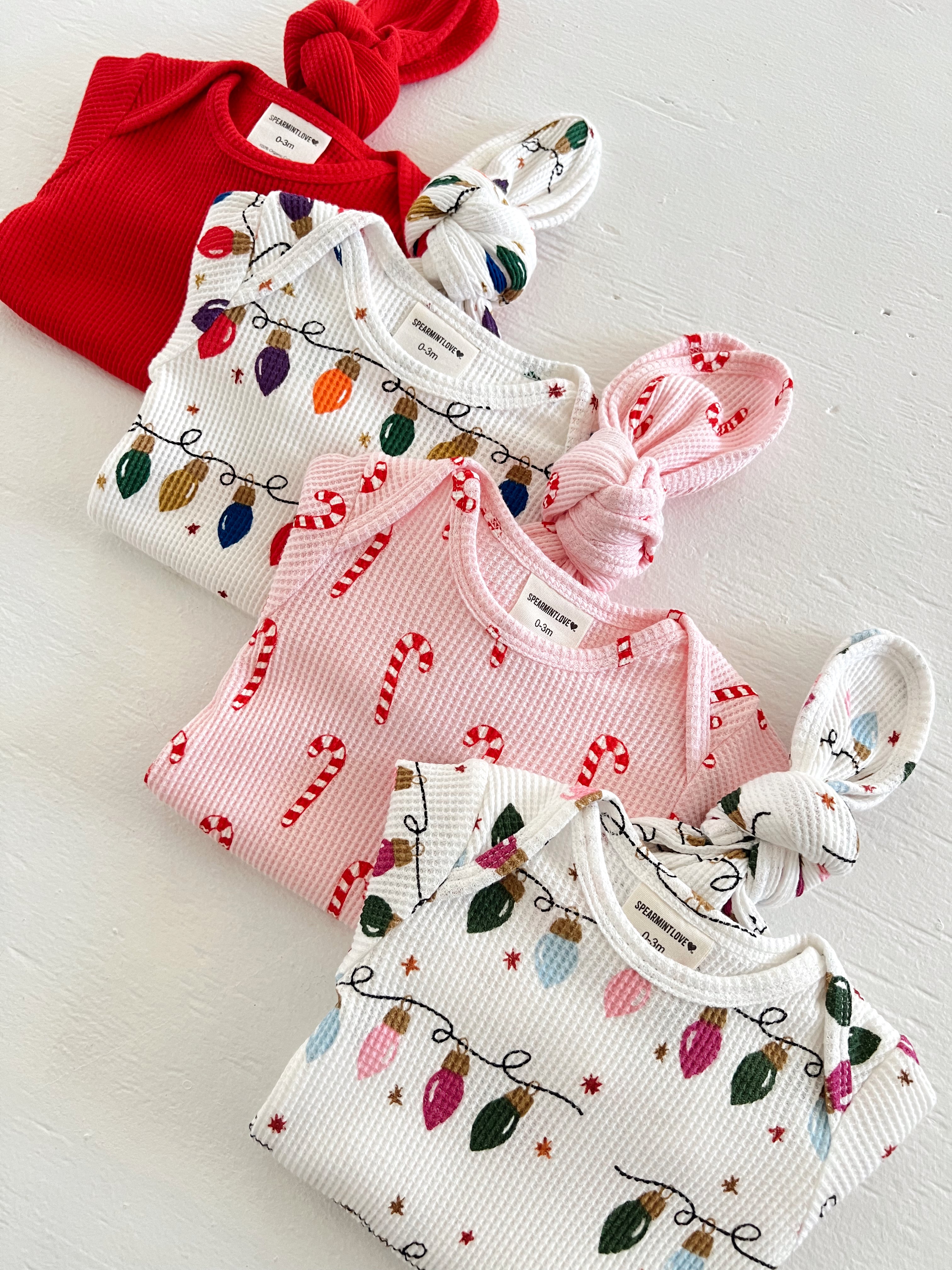 Colorful baby outfits featuring holiday patterns: red, candy cane, and Christmas lights.