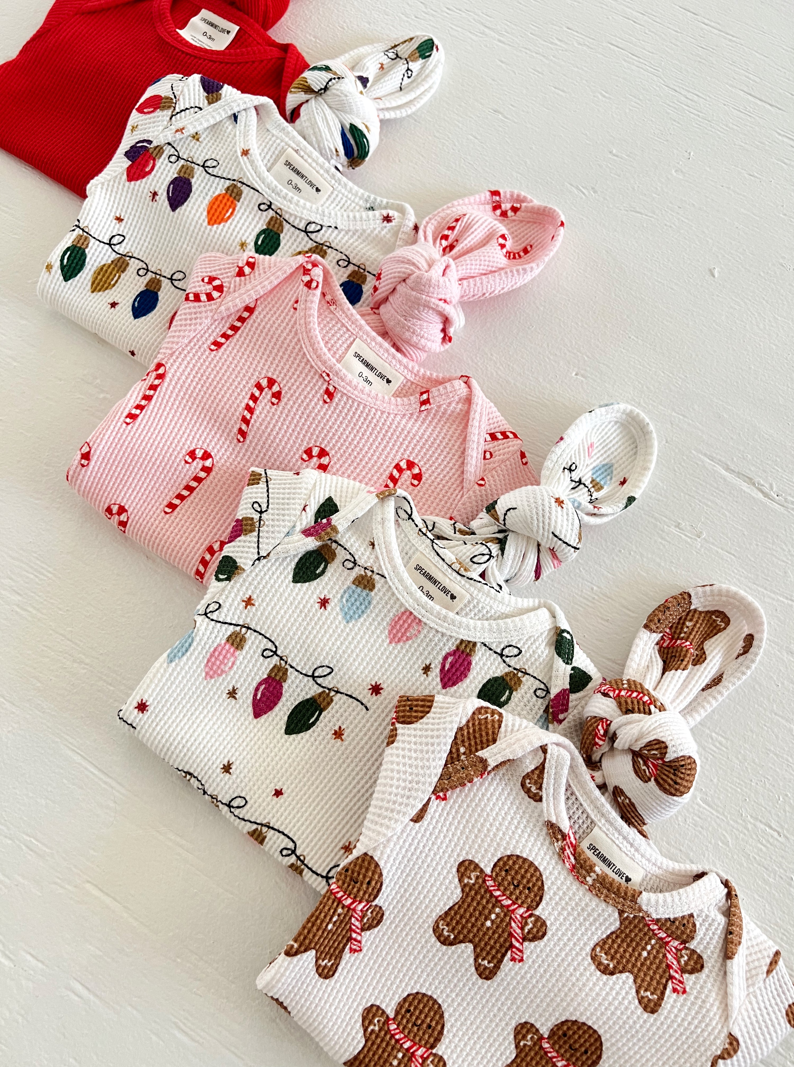 Colorful baby clothes in holiday patterns, including candy canes, lights, and gingerbread, laid out on a white surface.