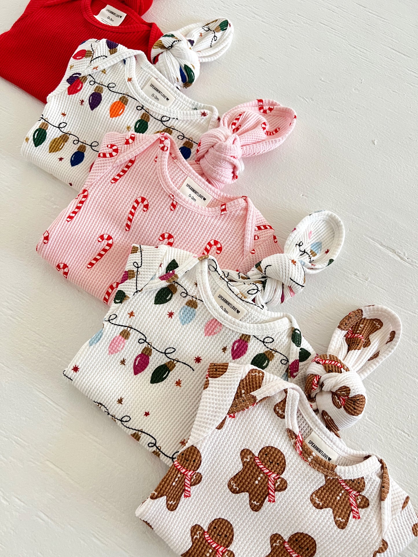 Colorful baby clothes in holiday patterns, including candy canes, lights, and gingerbread, laid out on a white surface.