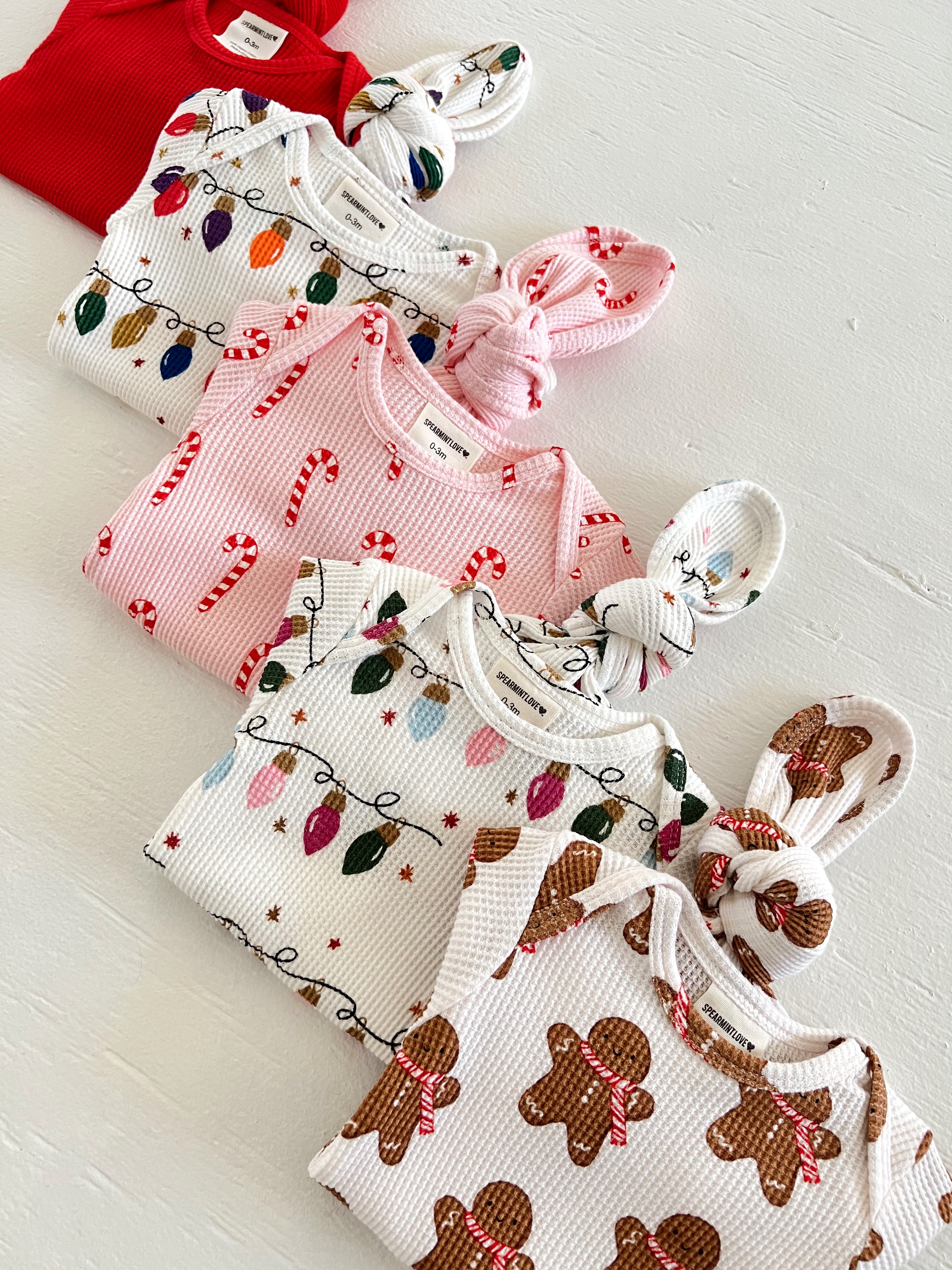 Colorful baby clothes in holiday patterns, including candy canes, lights, and gingerbread, laid out on a white surface.