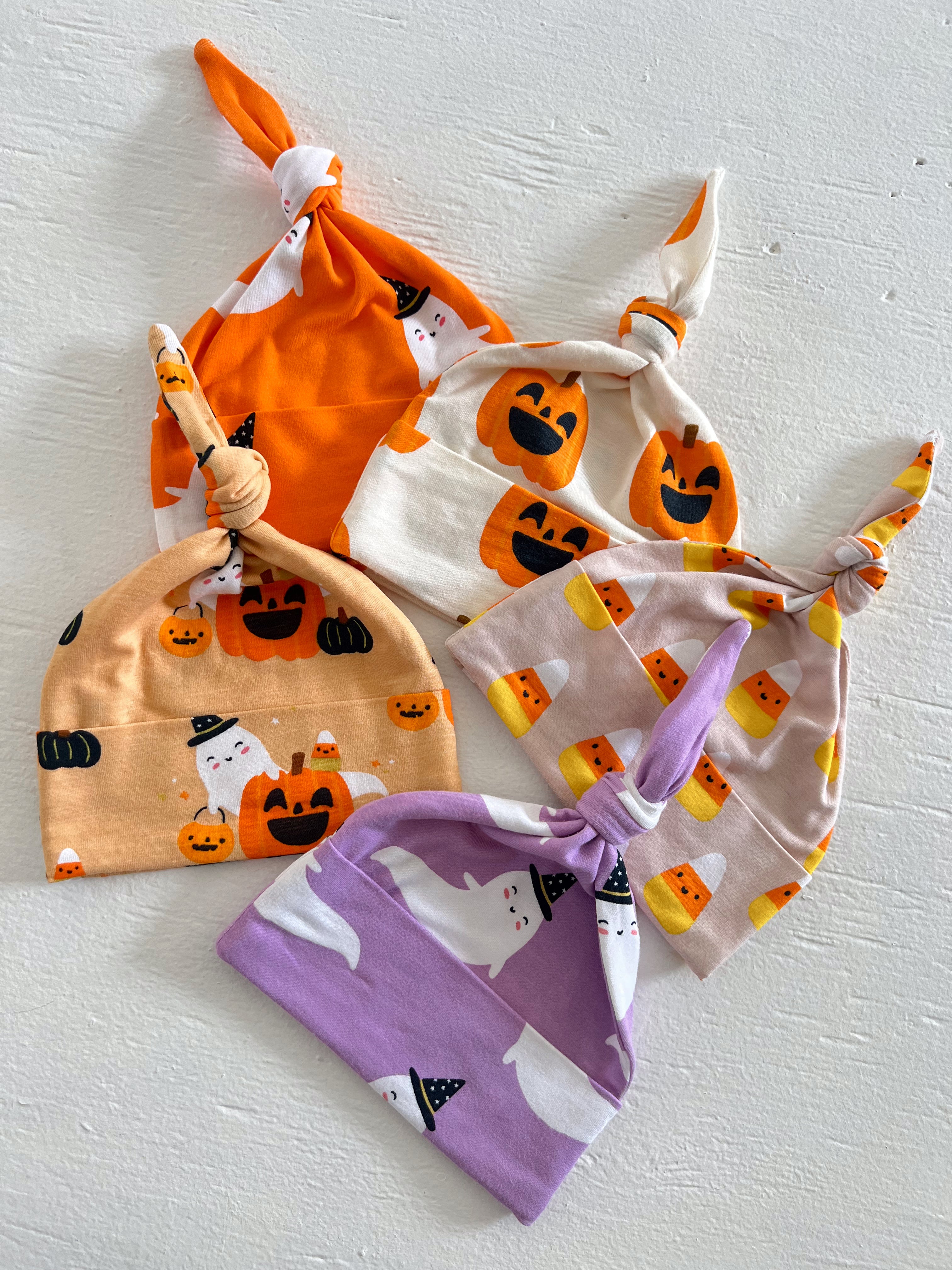 Four colorful Halloween-themed knot hats featuring ghosts, pumpkins, and candy corn on a white background.