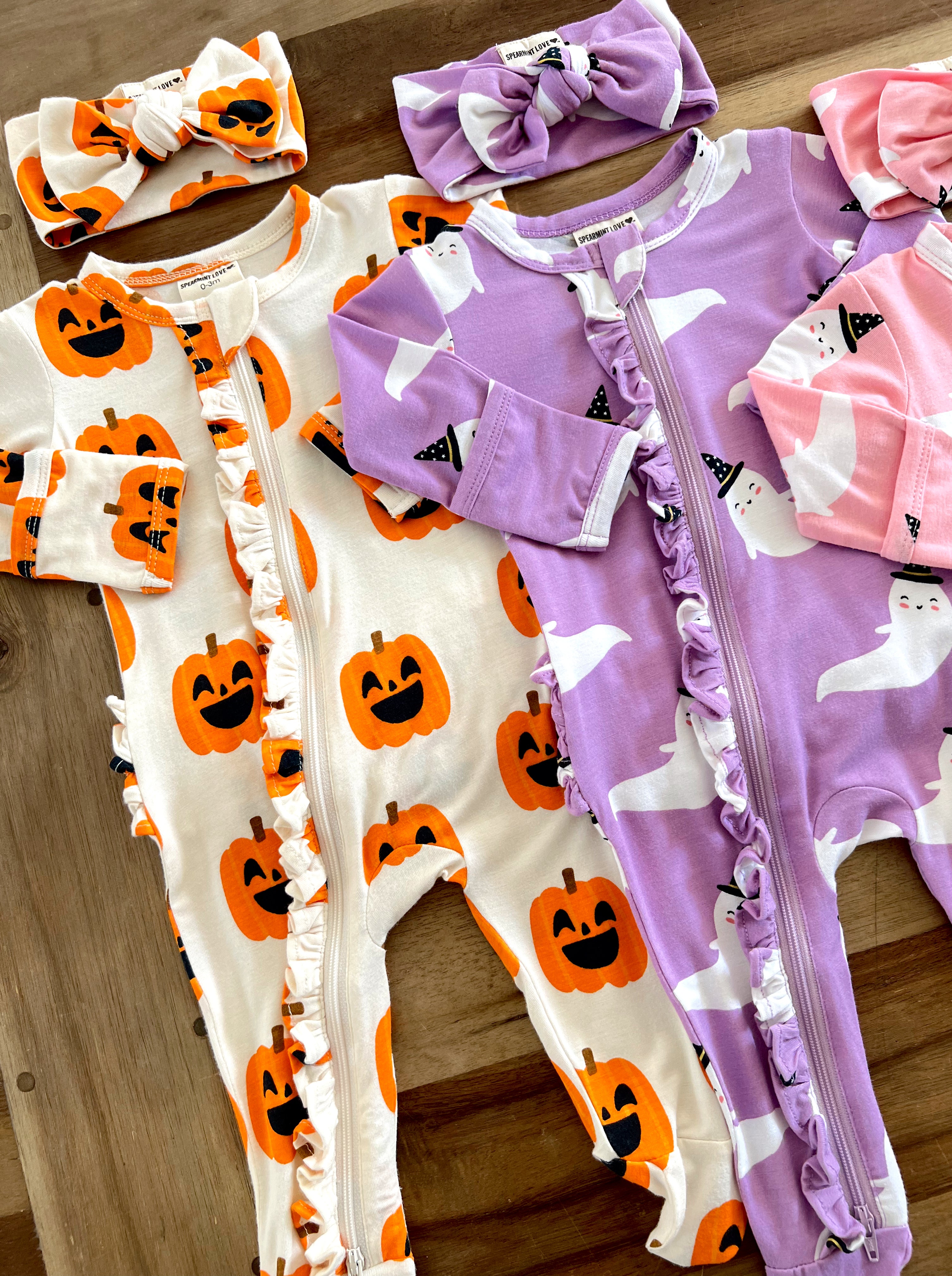 Two cozy Halloween onesies with pumpkin and ghost patterns, paired with matching headbands.