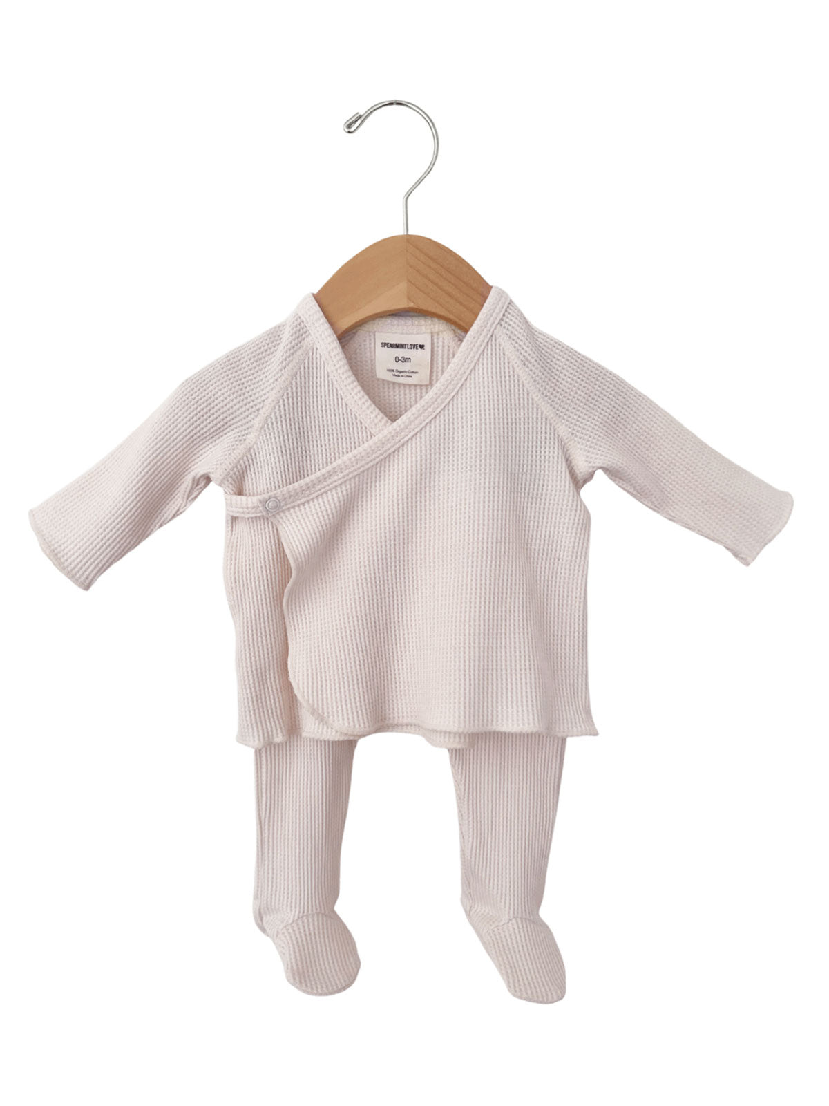 Pale pink newborn outfit with long sleeves, pants, and footed design, displayed on a wooden hanger.