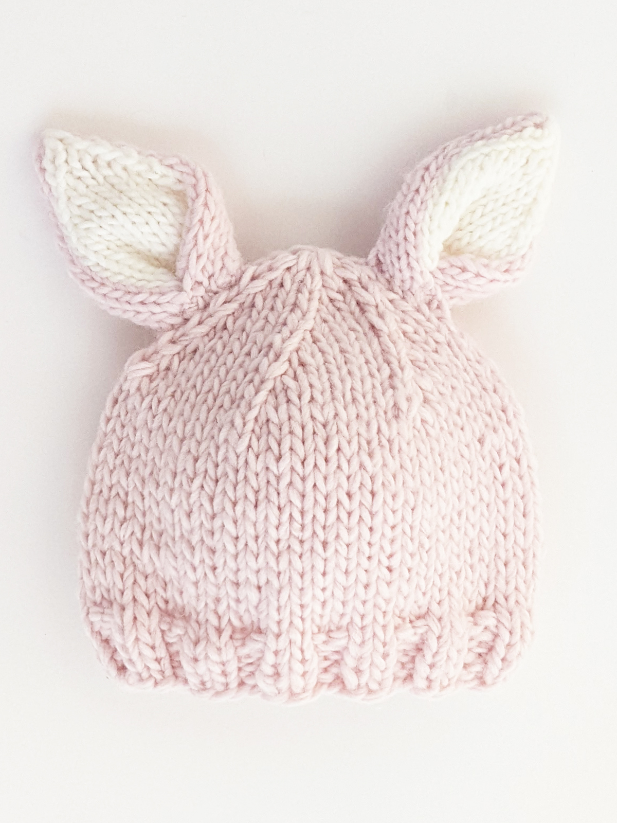 Pink knit bunny hat with white ears on a light background.
