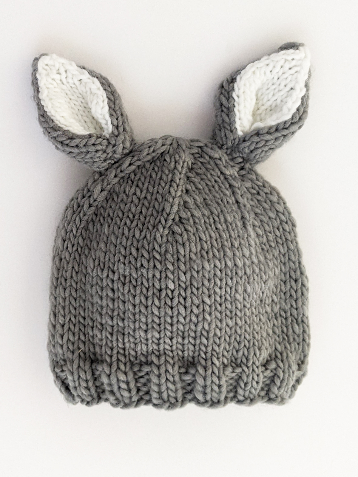 Gray knitted hat with white inner ears, resembling a bunny, displayed on a white background.