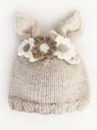 Beige knitted hat with bunny ears and floral accents on a white background. Perfect for infants and toddlers.