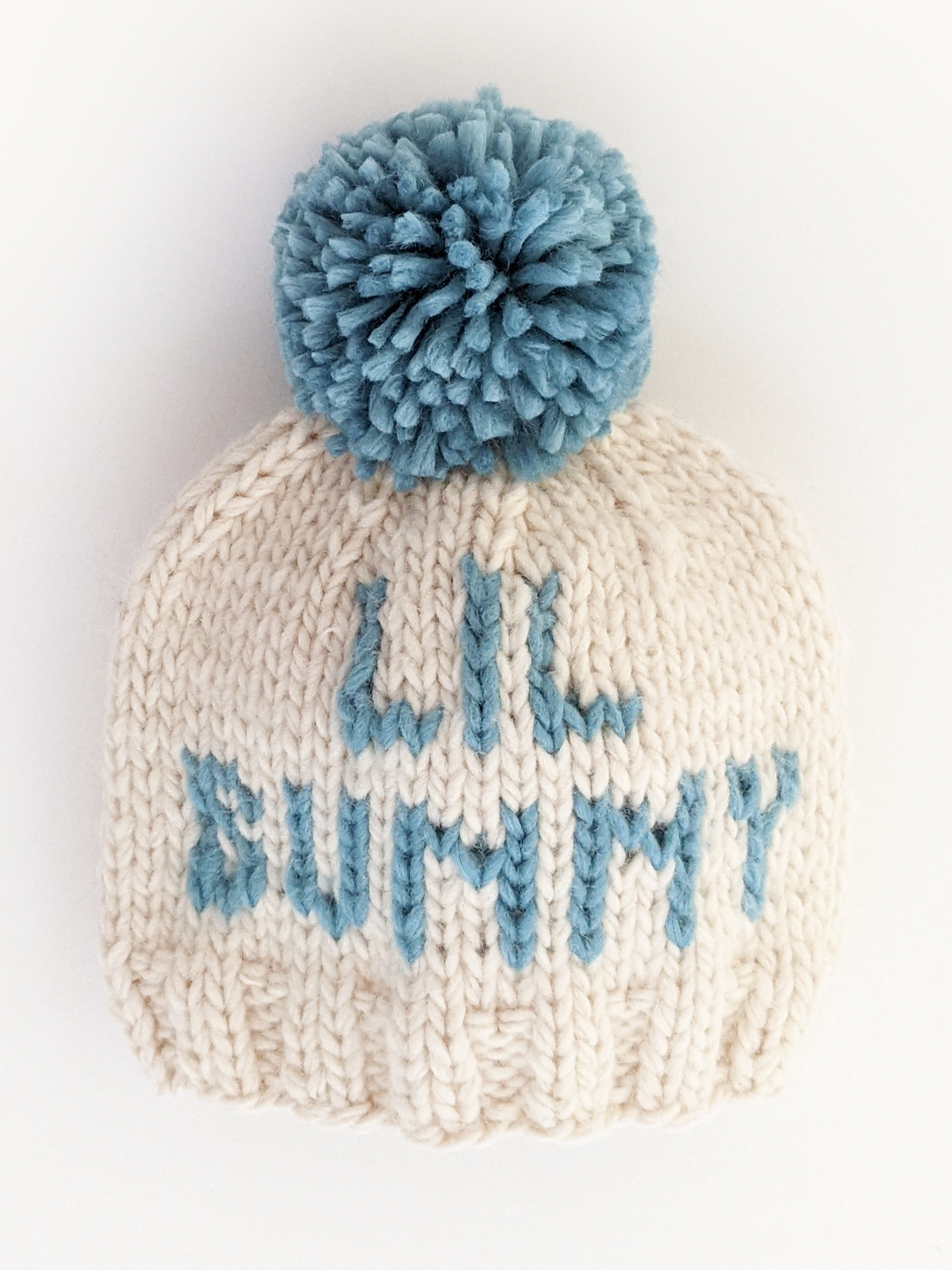 Knit cream hat with a blue pom-pom and "Lil Bunny" text on the front.