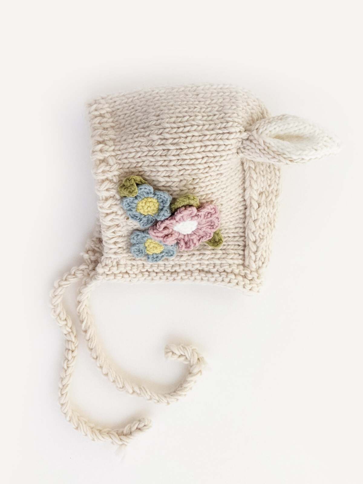 Knit baby bonnet with floral embroidery in pastel colors, featuring ties for securing under the chin.