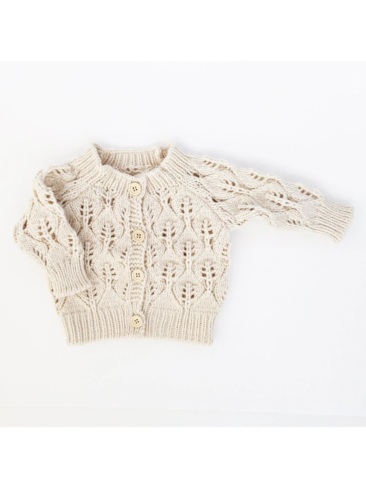 Cream knitted baby cardigan with a textured leaf pattern and wooden buttons.