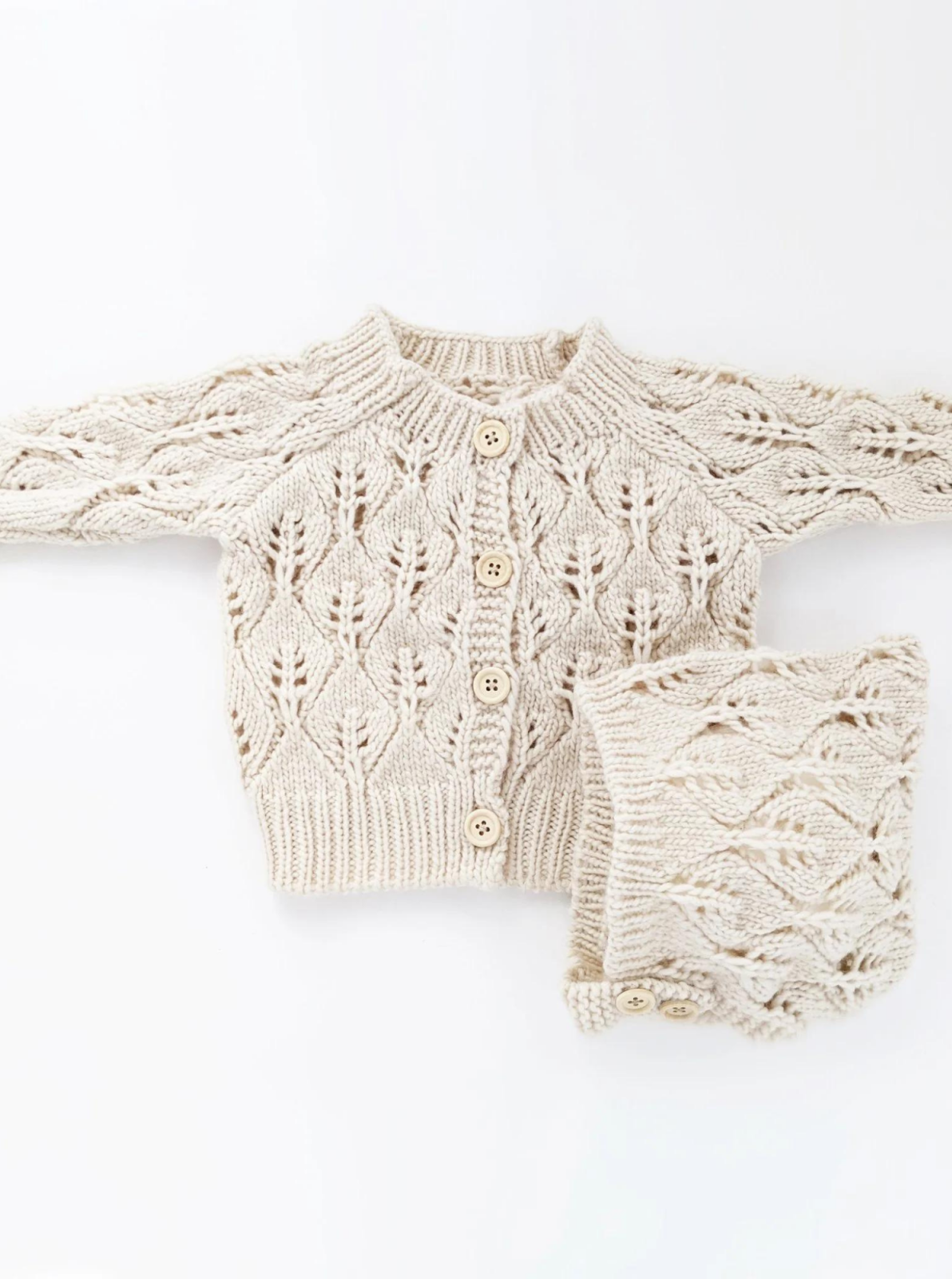 Cream-colored knitted cardigan and matching accessory, featuring a leaf pattern and wooden buttons.