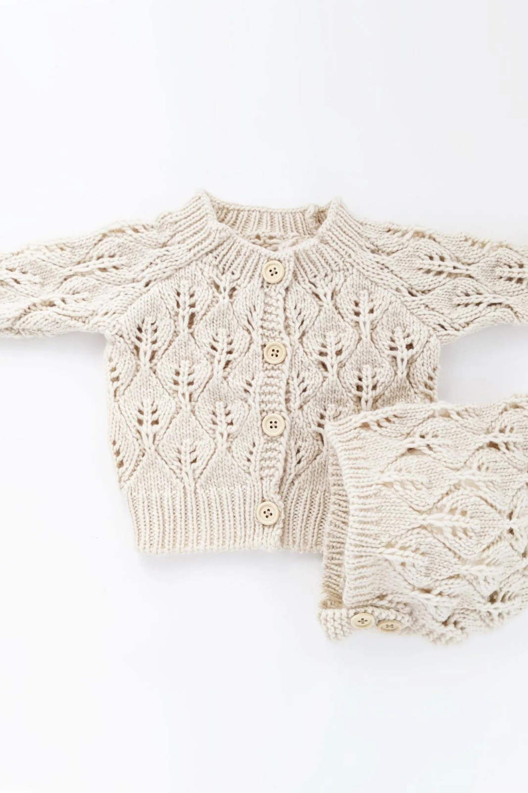 Cream-colored knitted cardigan and matching accessory, featuring a leaf pattern and wooden buttons.