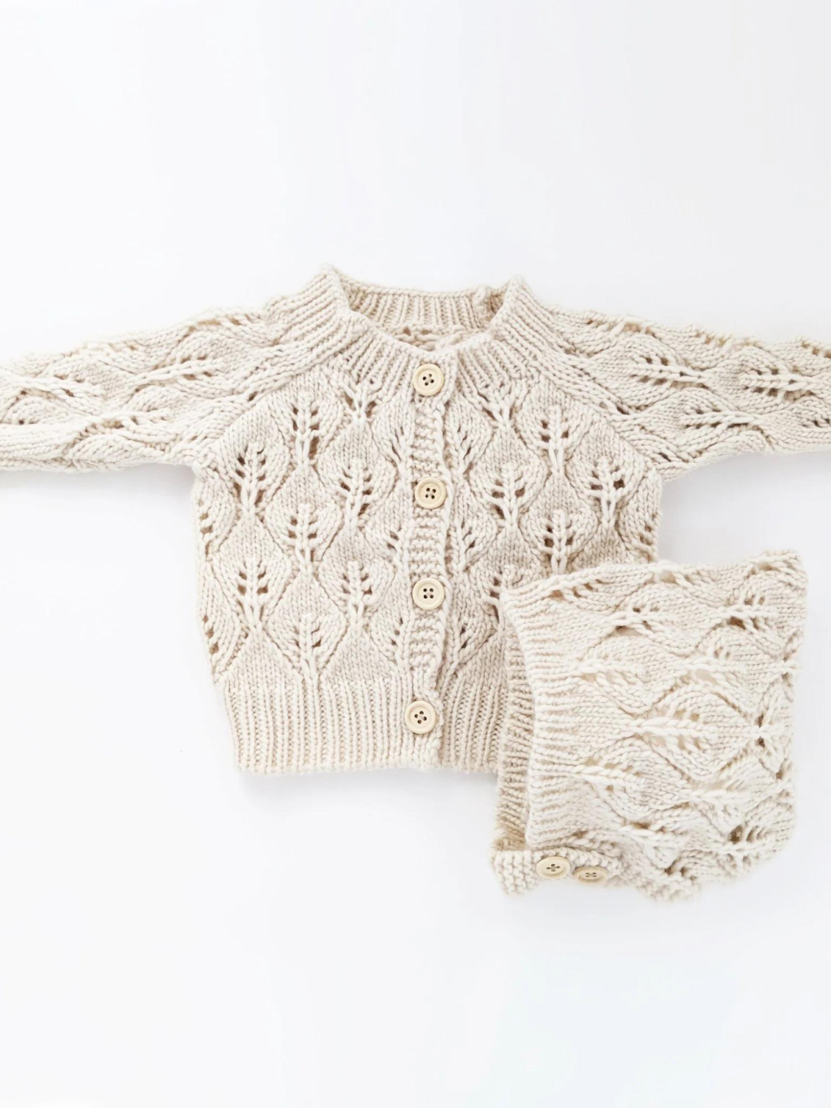 Cream-colored knitted cardigan and matching accessory, featuring a leaf pattern and wooden buttons.