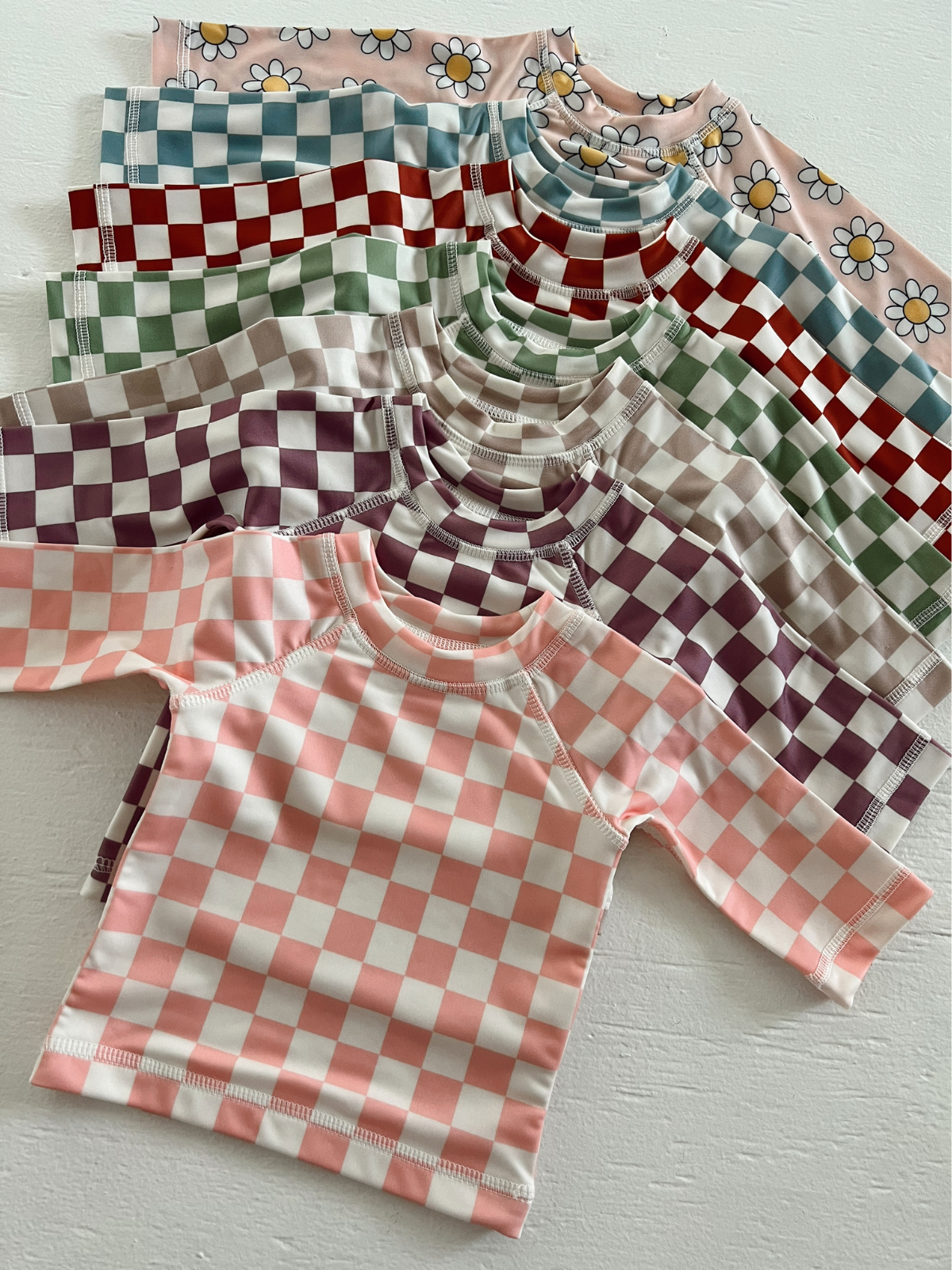 Colorful children’s shirts in various checker patterns and floral designs arranged on a white surface.