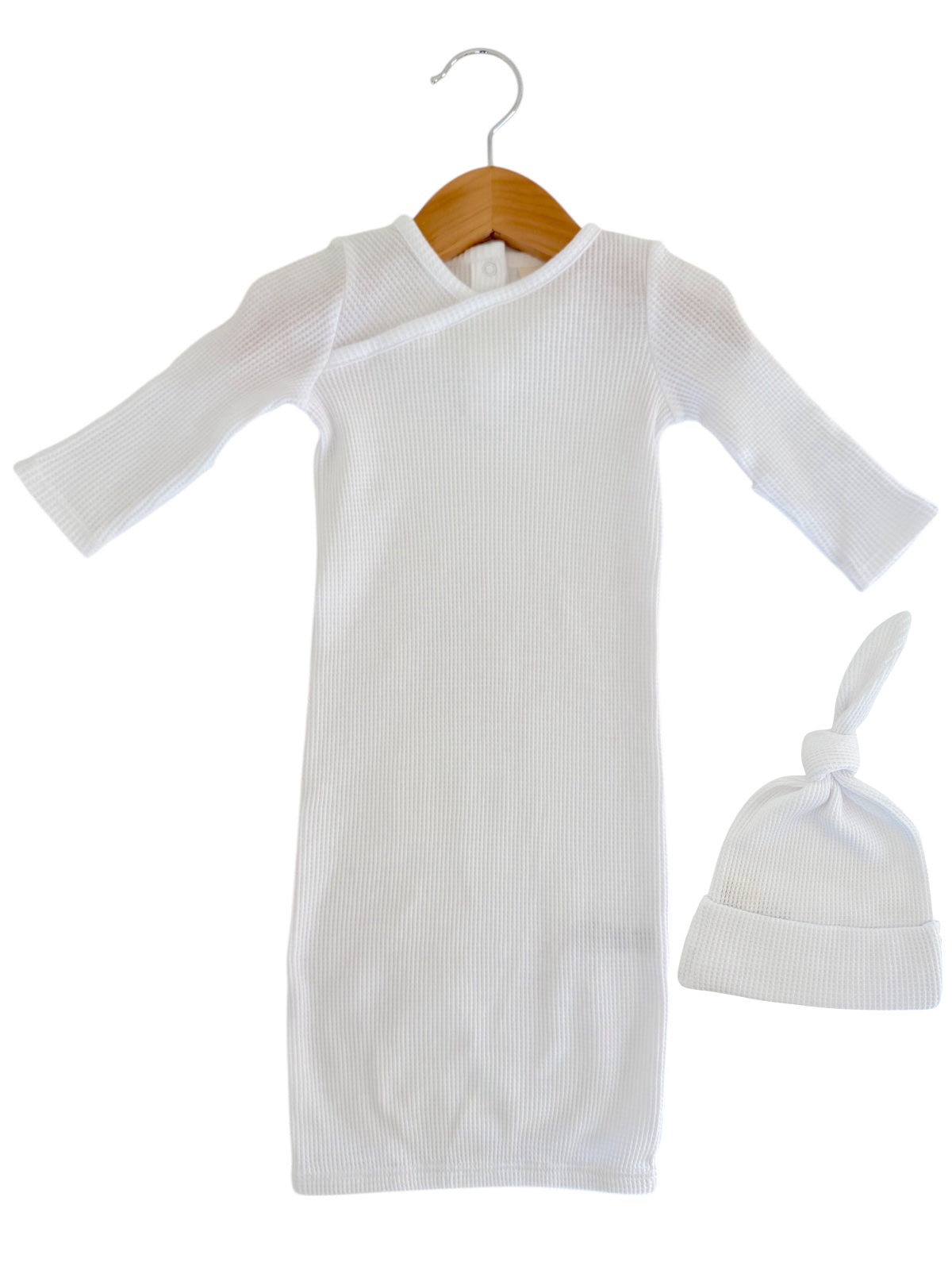 White ribbed baby gown with long sleeves and matching knot hat, displayed on a wooden hanger.