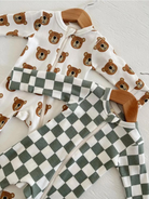Two baby onesies, one with bear print and the other in green checkered pattern, hanging on wooden hangers.