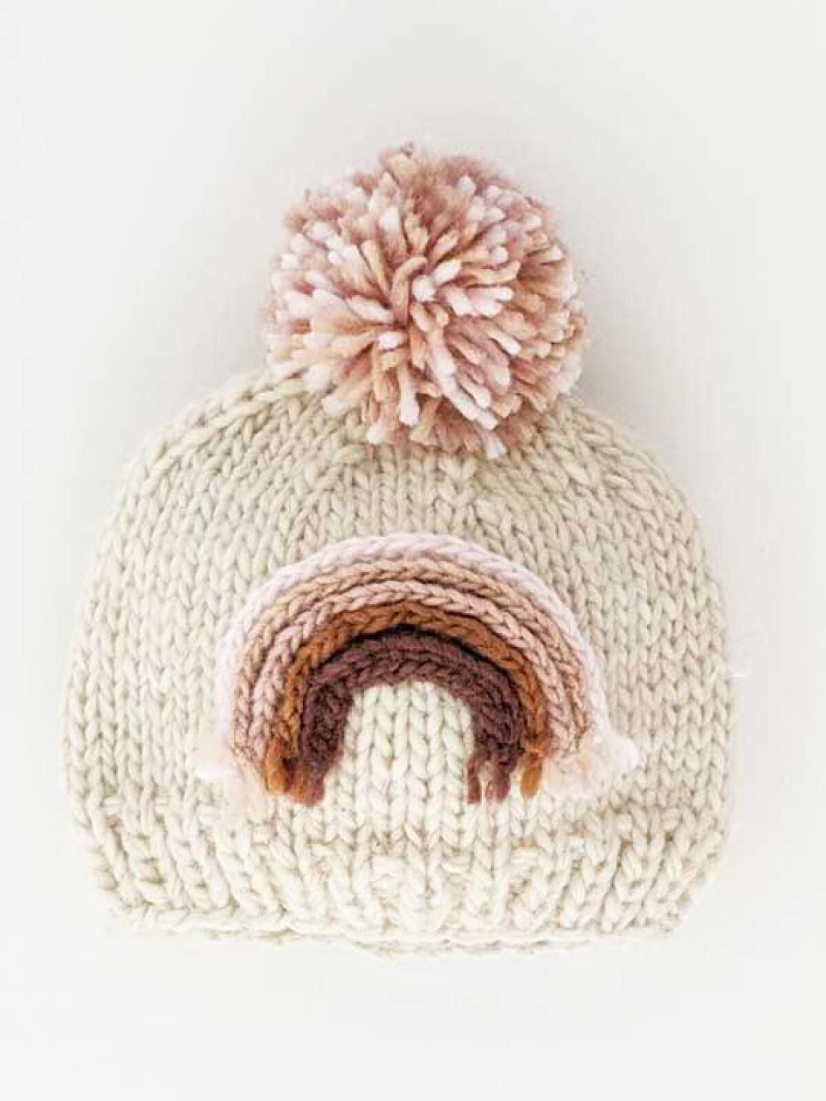 Knitted cream beanie with a pom-pom and a colorful rainbow design on the front.