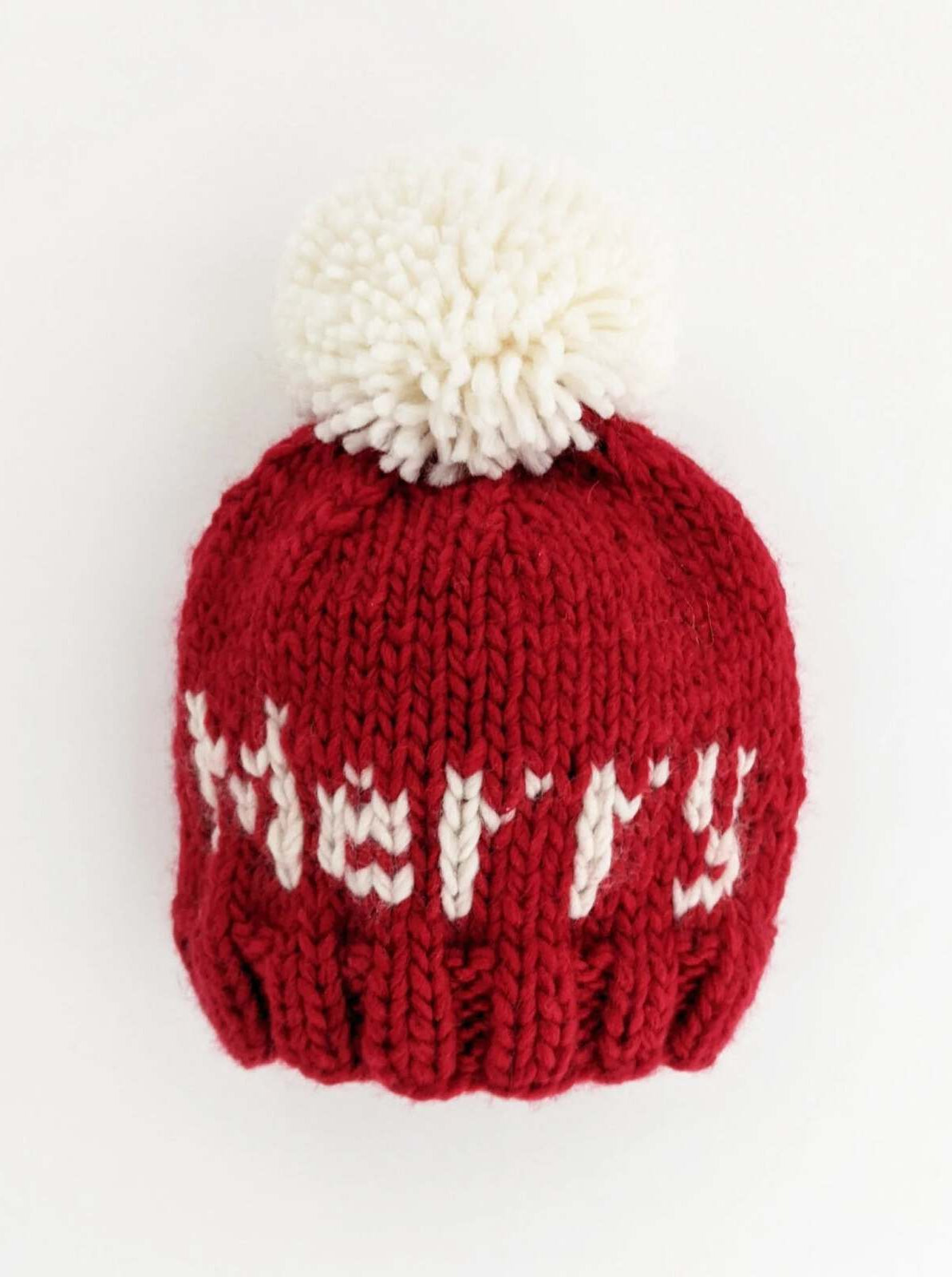 Red knitted winter hat with a fluffy white pom-pom and the word "Merry" stitched in white.