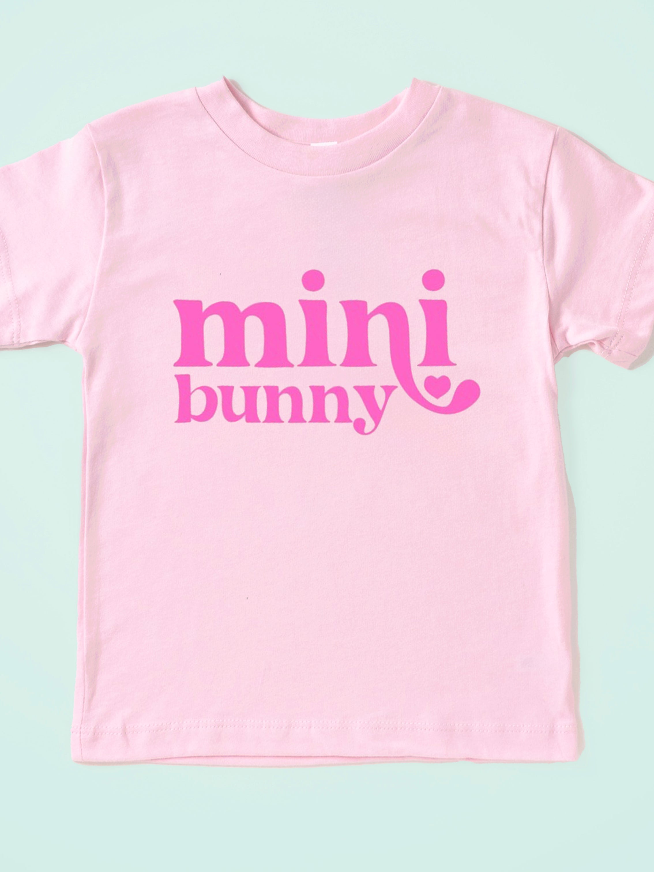 Light pink t-shirt with the text "mini bunny" in bold pink letters, featuring a heart accent.