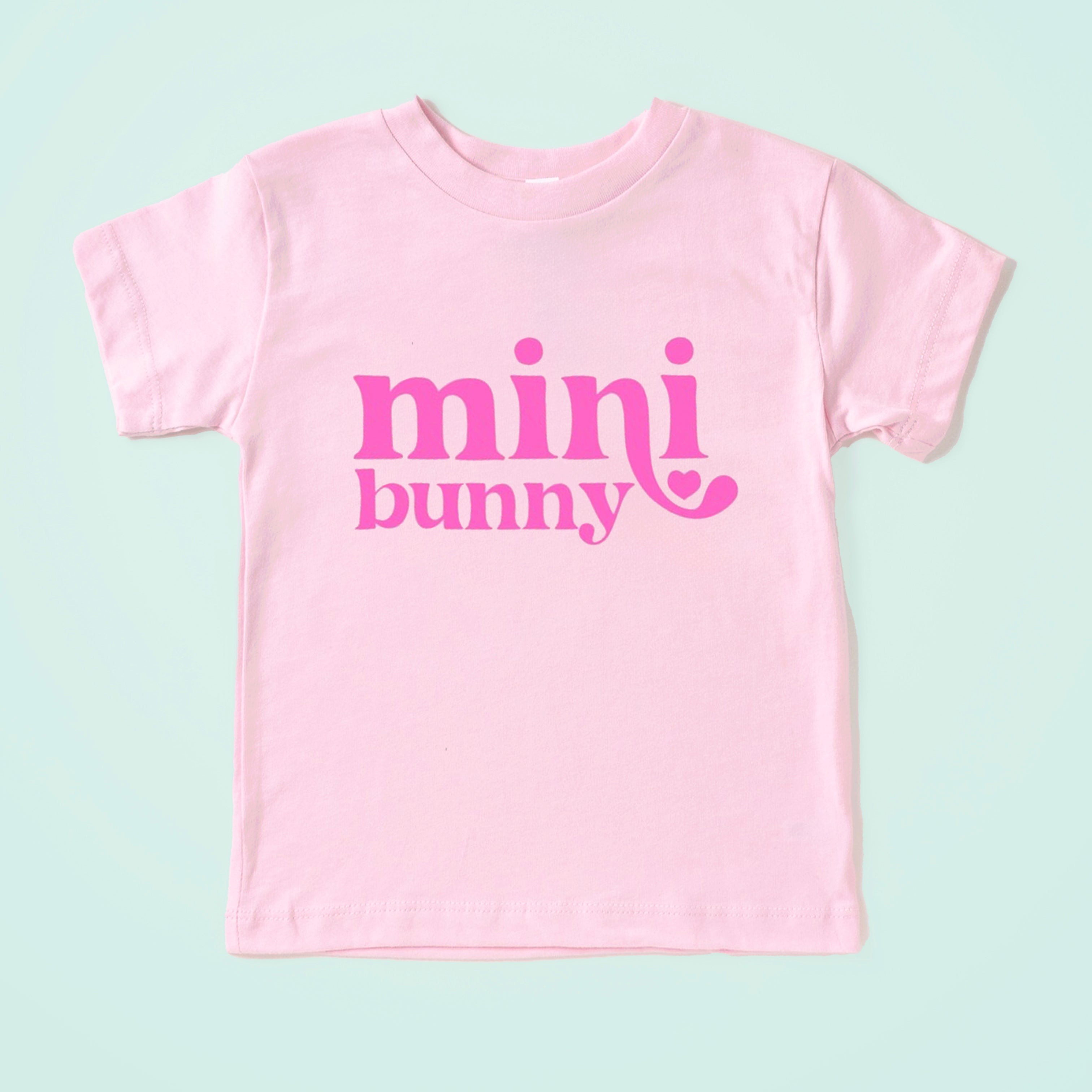 Light pink t-shirt with the text "mini bunny" in bold pink letters, featuring a heart accent.