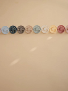 A row of colorful pacifiers displayed on a light beige background.