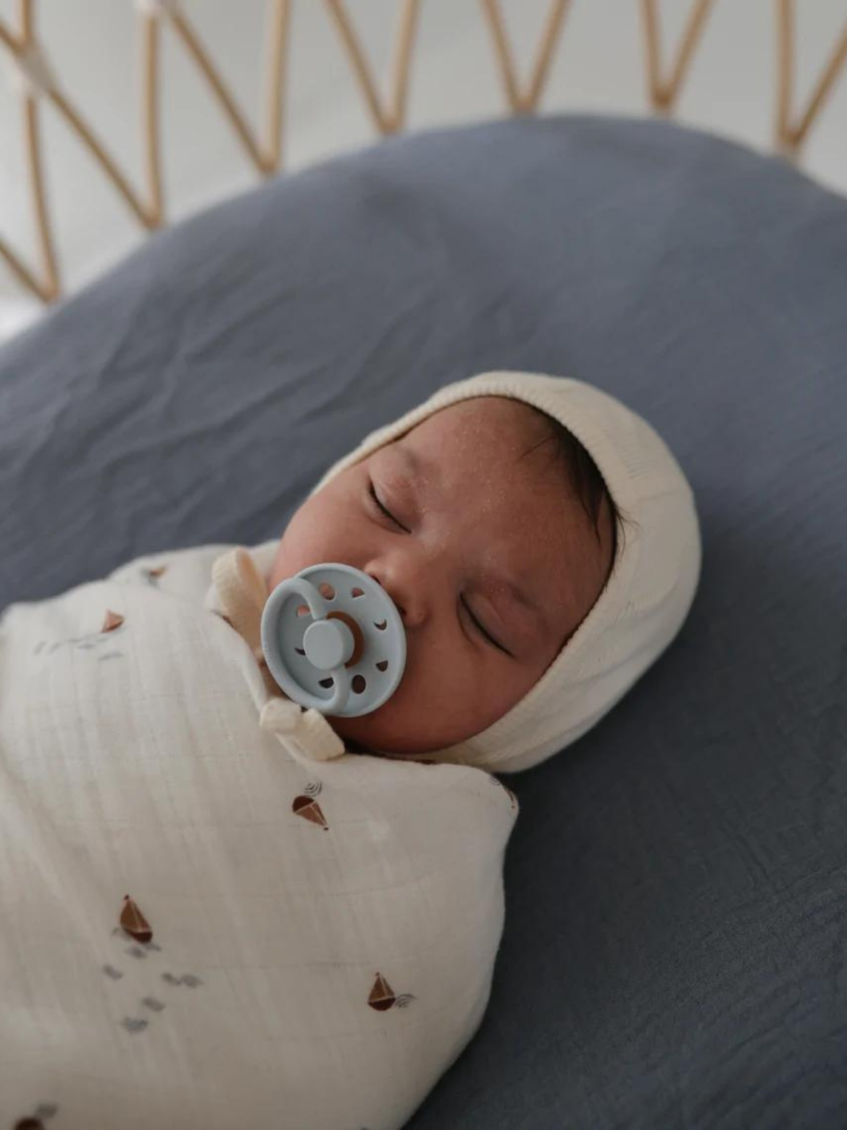 Infant peacefully sleeping wrapped in a blanket with a pacifier, on a soft bedding surface.