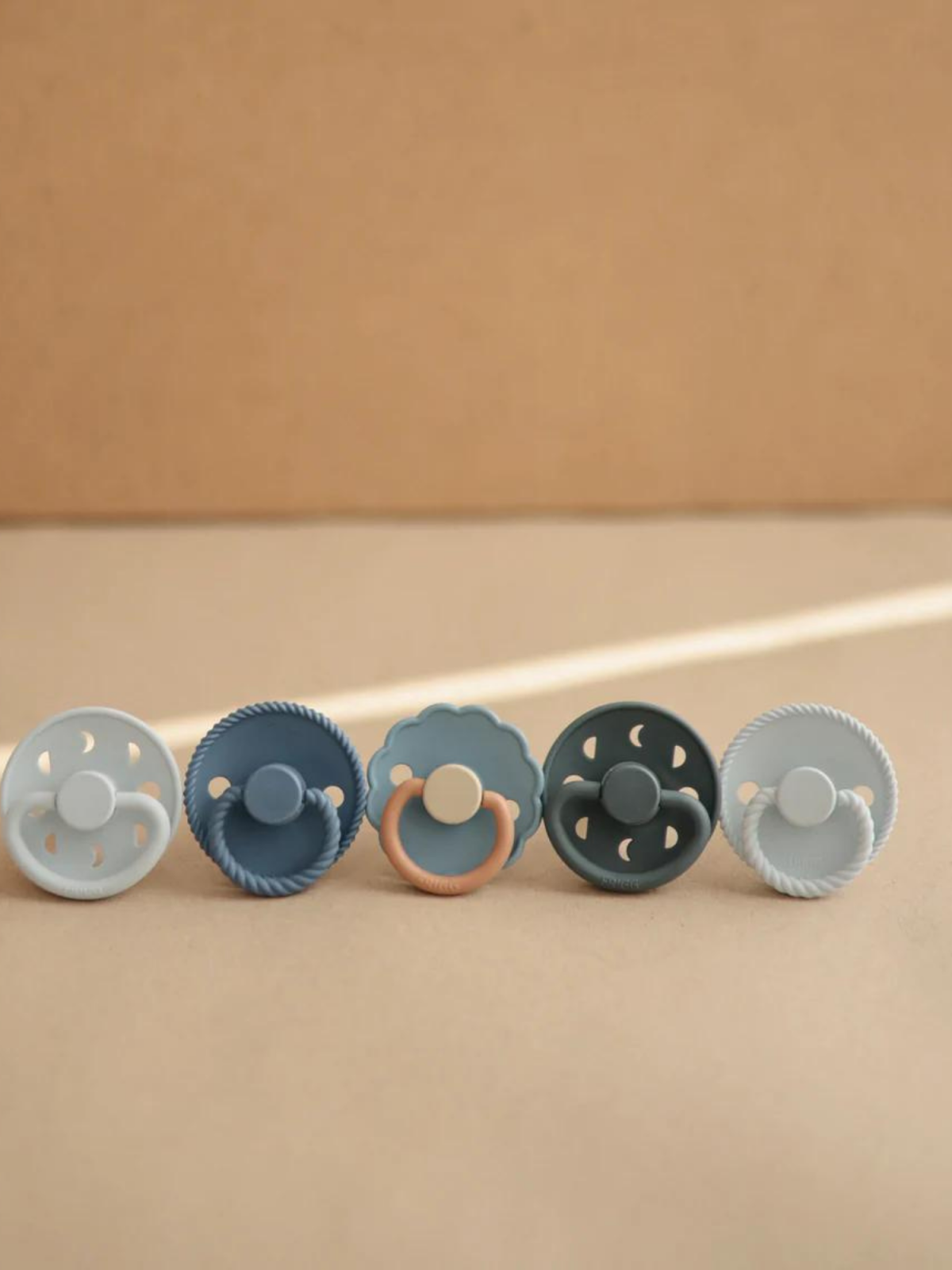 Five colorful baby pacifiers arranged in a row against a neutral background.