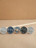Five colorful baby pacifiers arranged in a row against a neutral background.