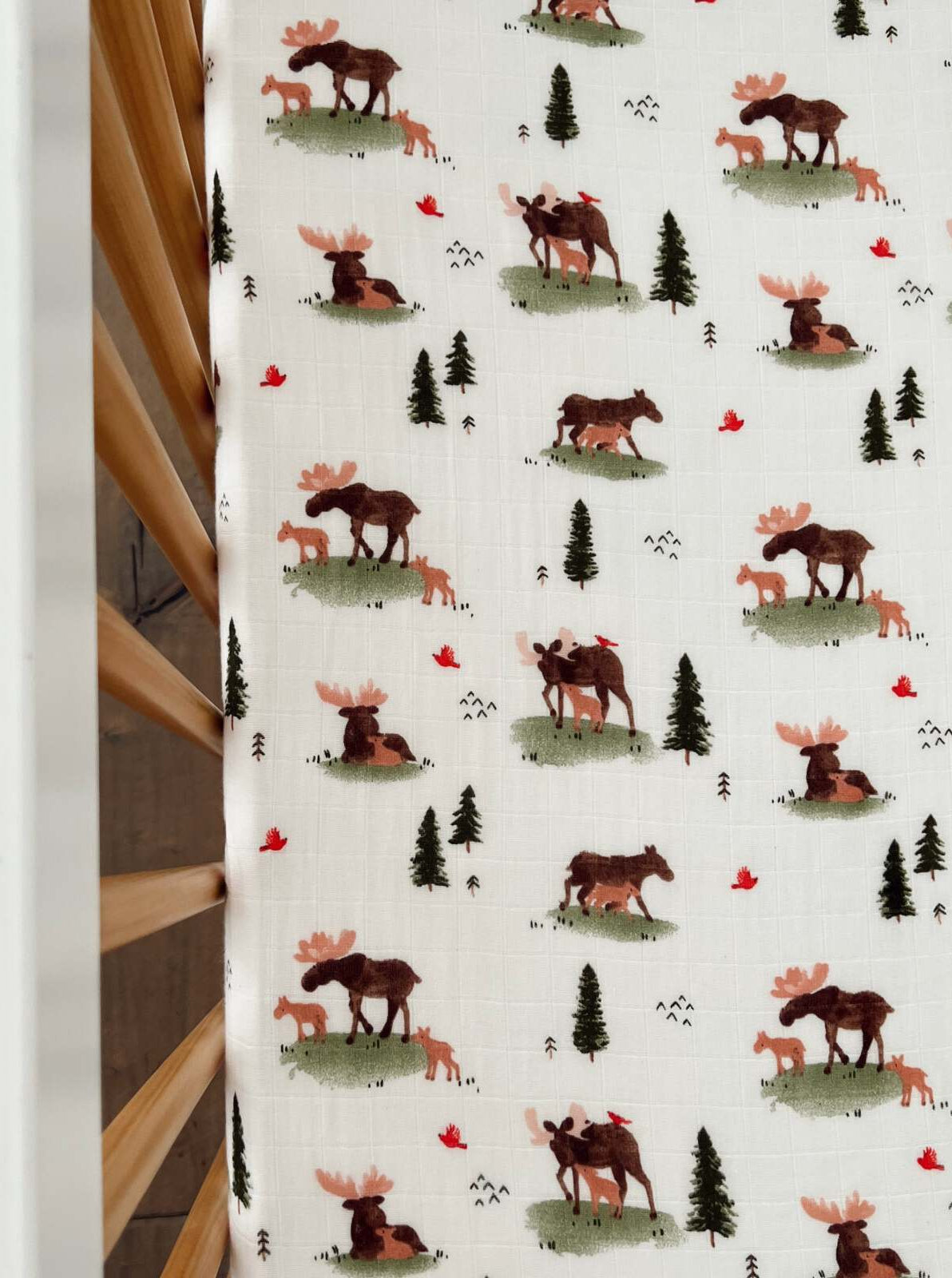 Patterned fabric featuring moose, foxes, red birds, and evergreen trees on a light background.
