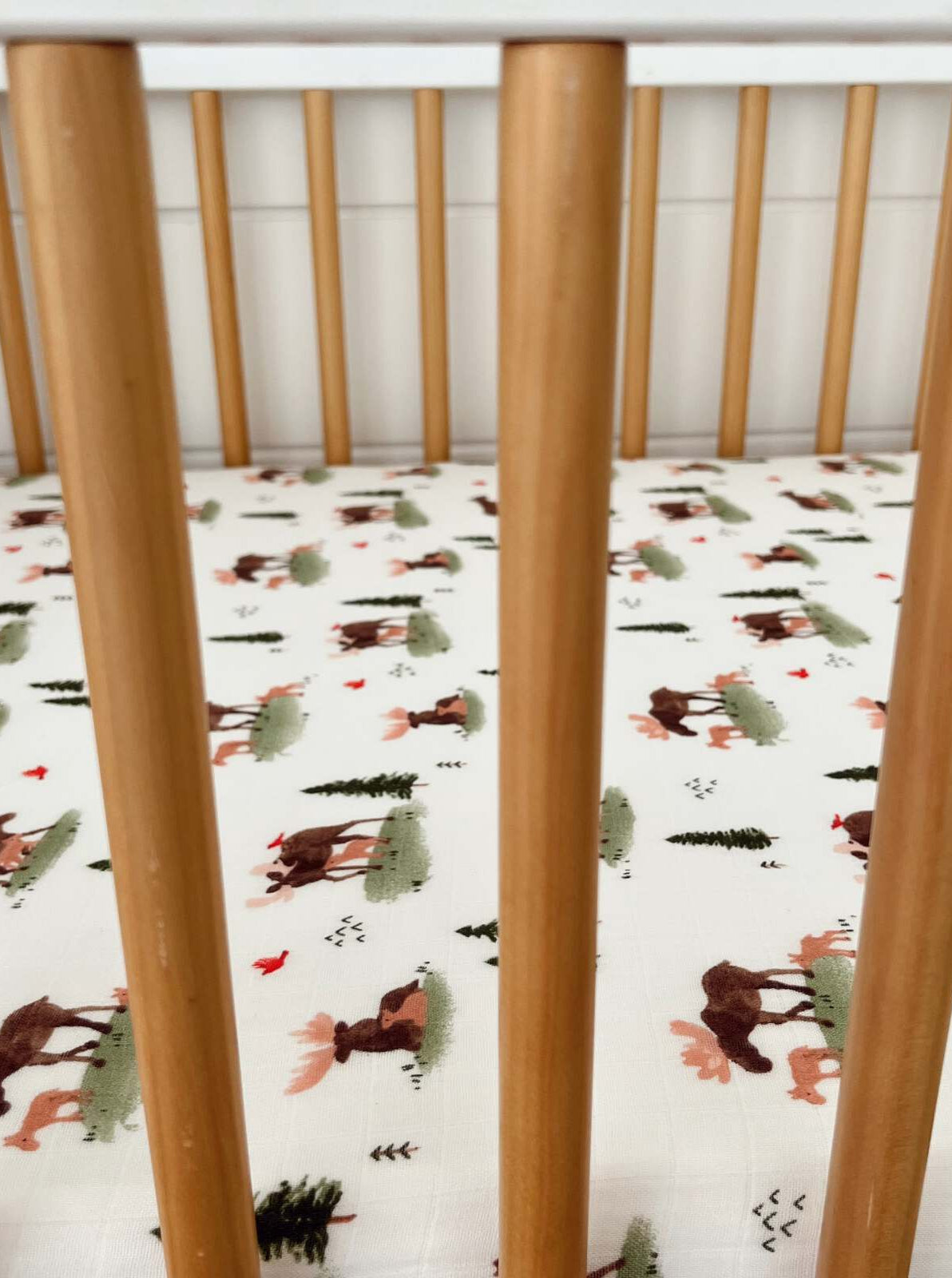 Wooden crib rails with a playful fabric featuring moose and trees in soft colors.