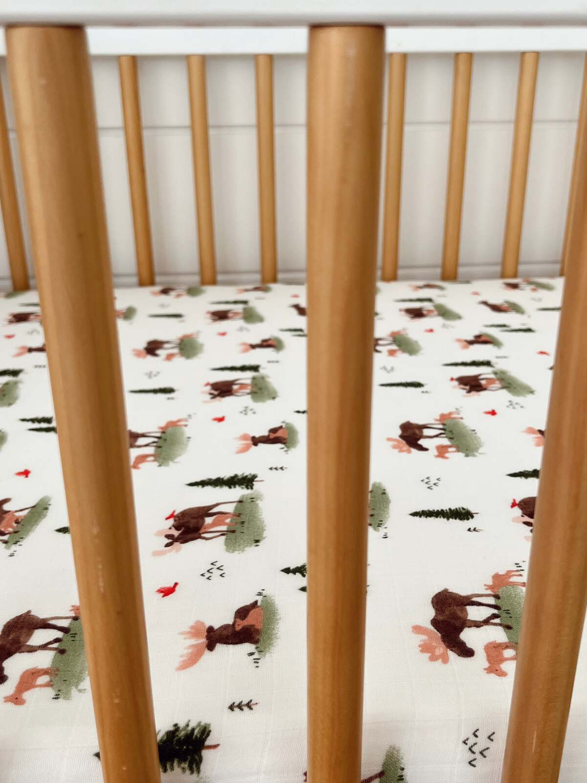 Wooden crib rails with a playful fabric featuring moose and trees in soft colors.