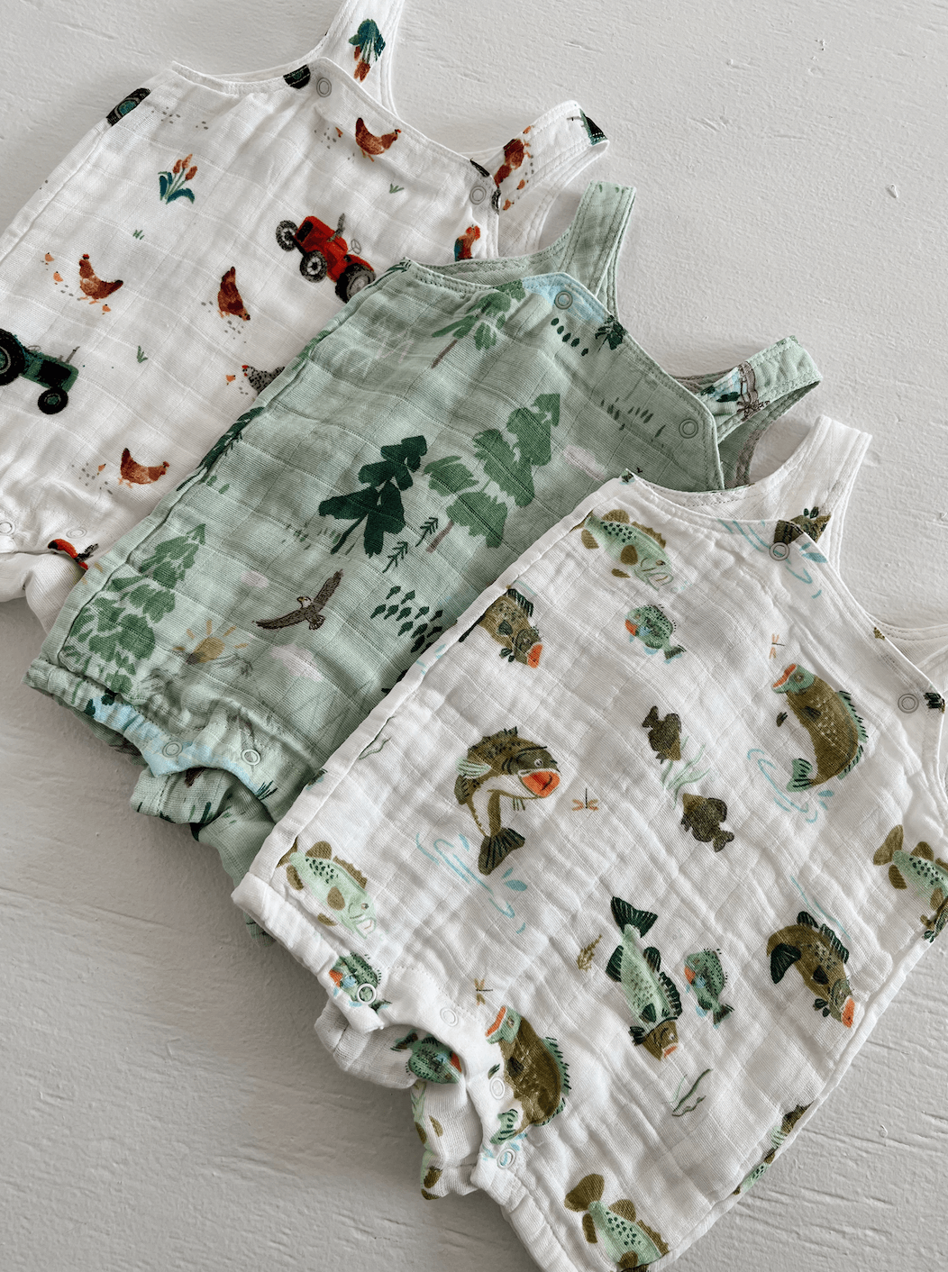 Three children’s romper outfits: one with chickens, one with trees, and one with fish patterns on a light background.