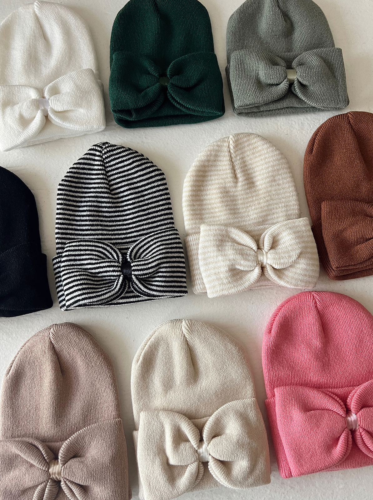 Assorted beanies in various colors and styles, featuring bows, arranged on a white background.