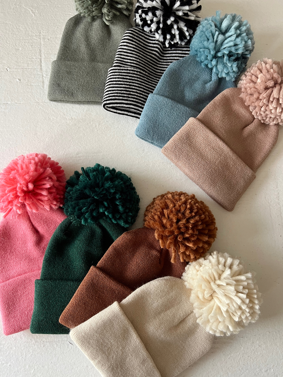 Colorful winter beanies with pom-poms arranged neatly on a light surface.
