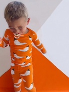 Young child in orange ghost-patterned pajamas, smiling against a colorful background.