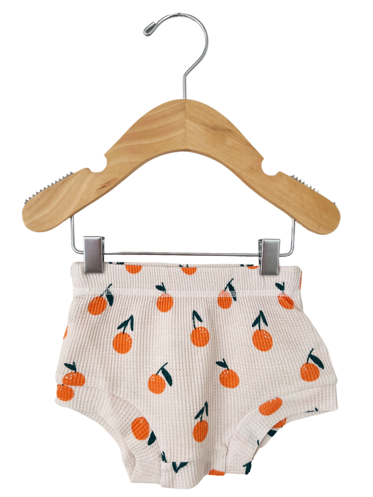 Children's shorts with orange patterns hanging on a wooden hanger against a white background.