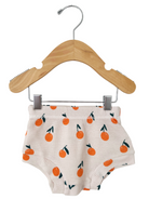 Children's shorts with orange patterns hanging on a wooden hanger against a white background.